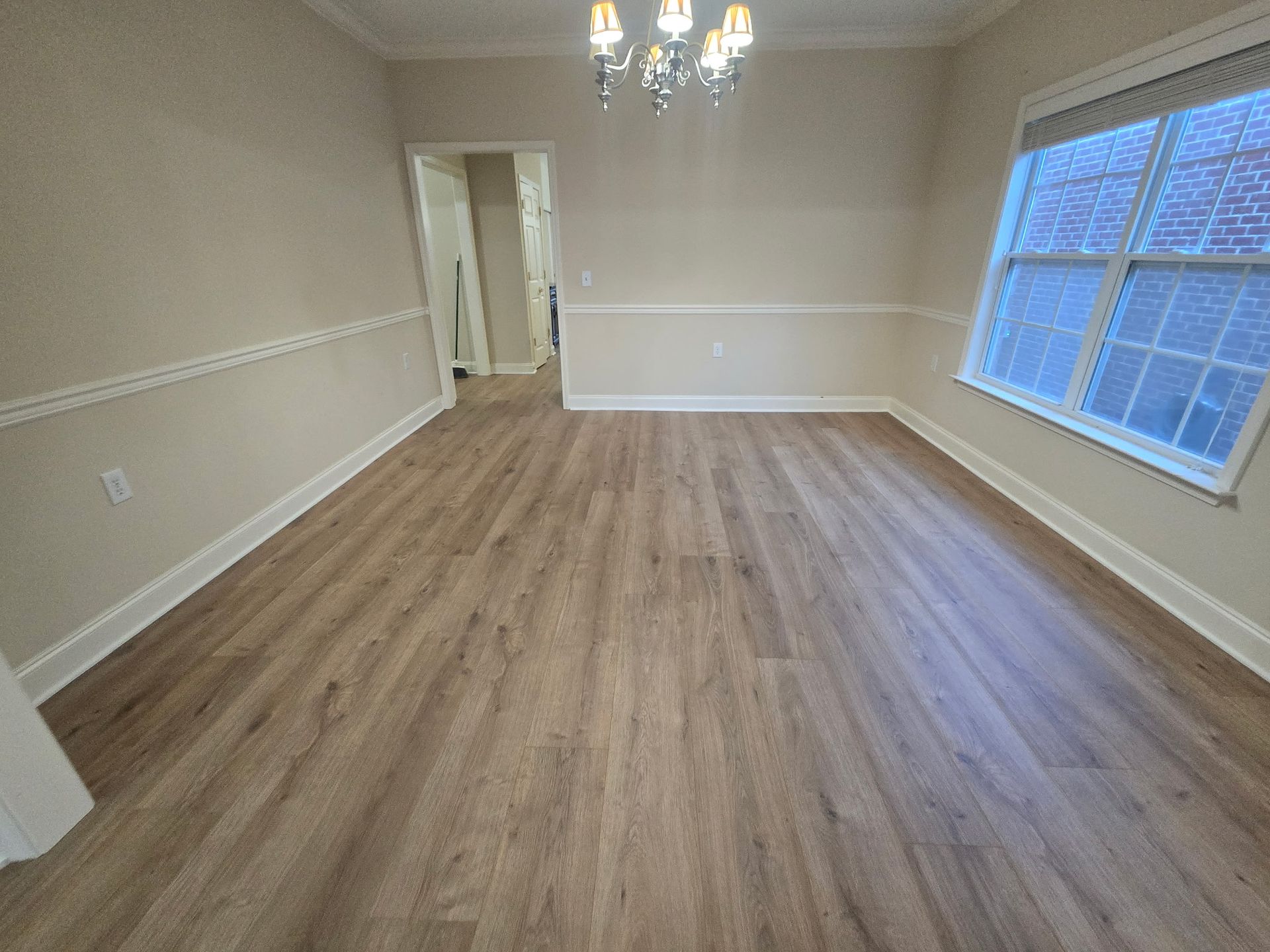 Empty dining room with wood flooring, chandelier, and a large window.