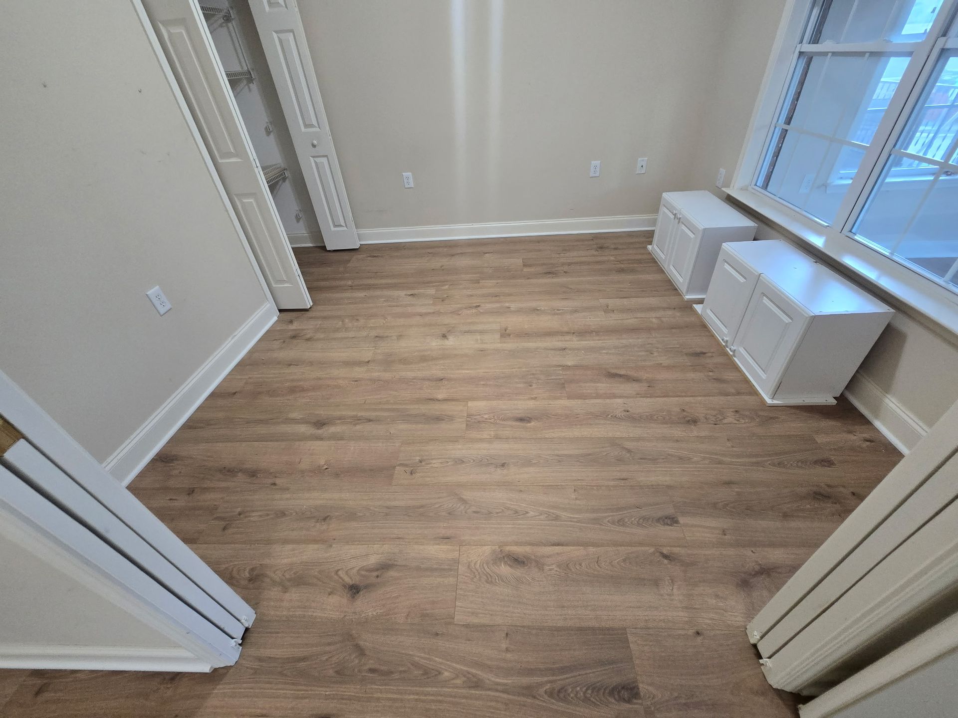 Bedroom with wood-look flooring, two white cabinets by a window, and open doorways.