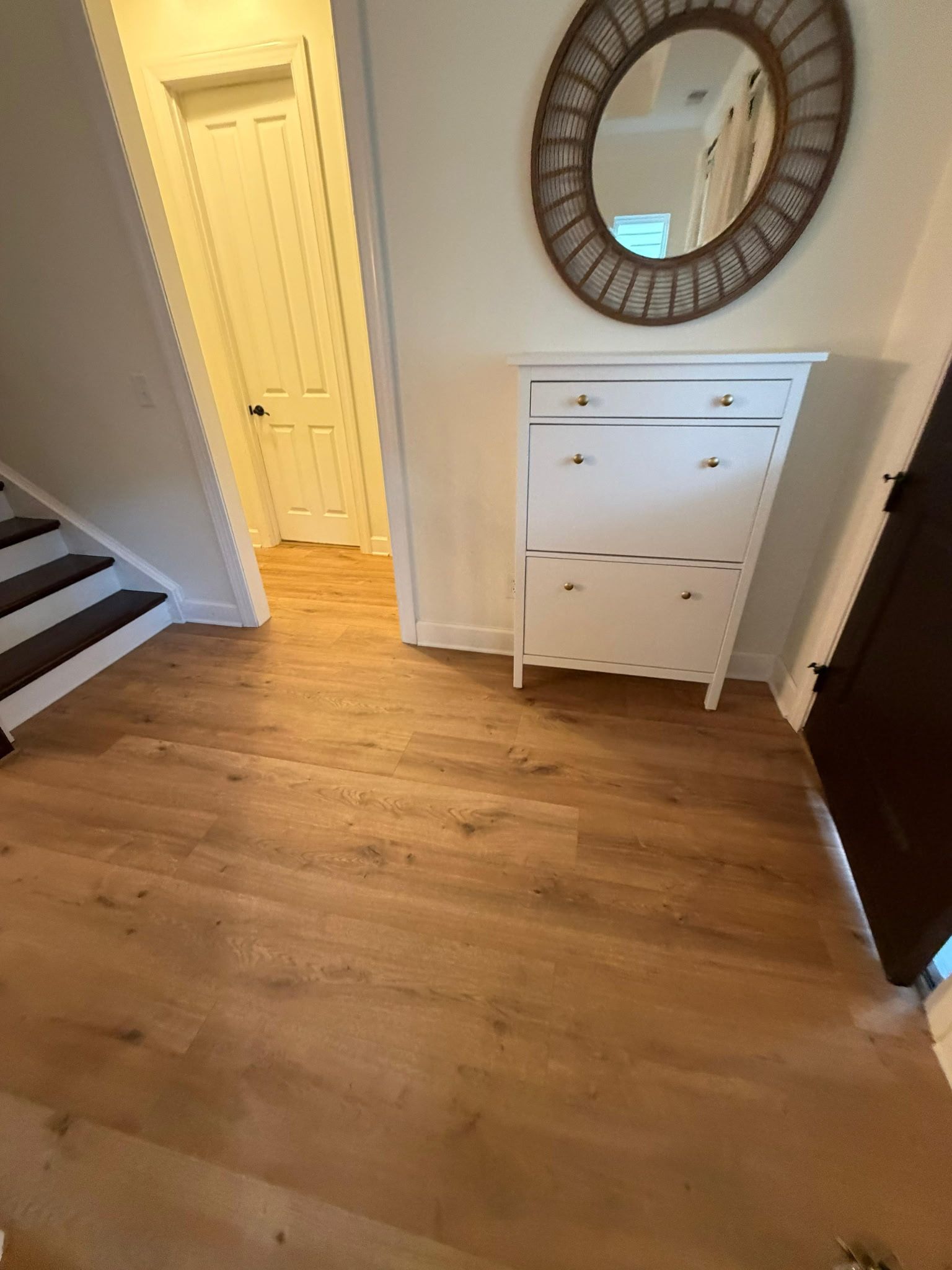 Entryway with wood floors, white cabinet, round mirror, door, and stairs.
