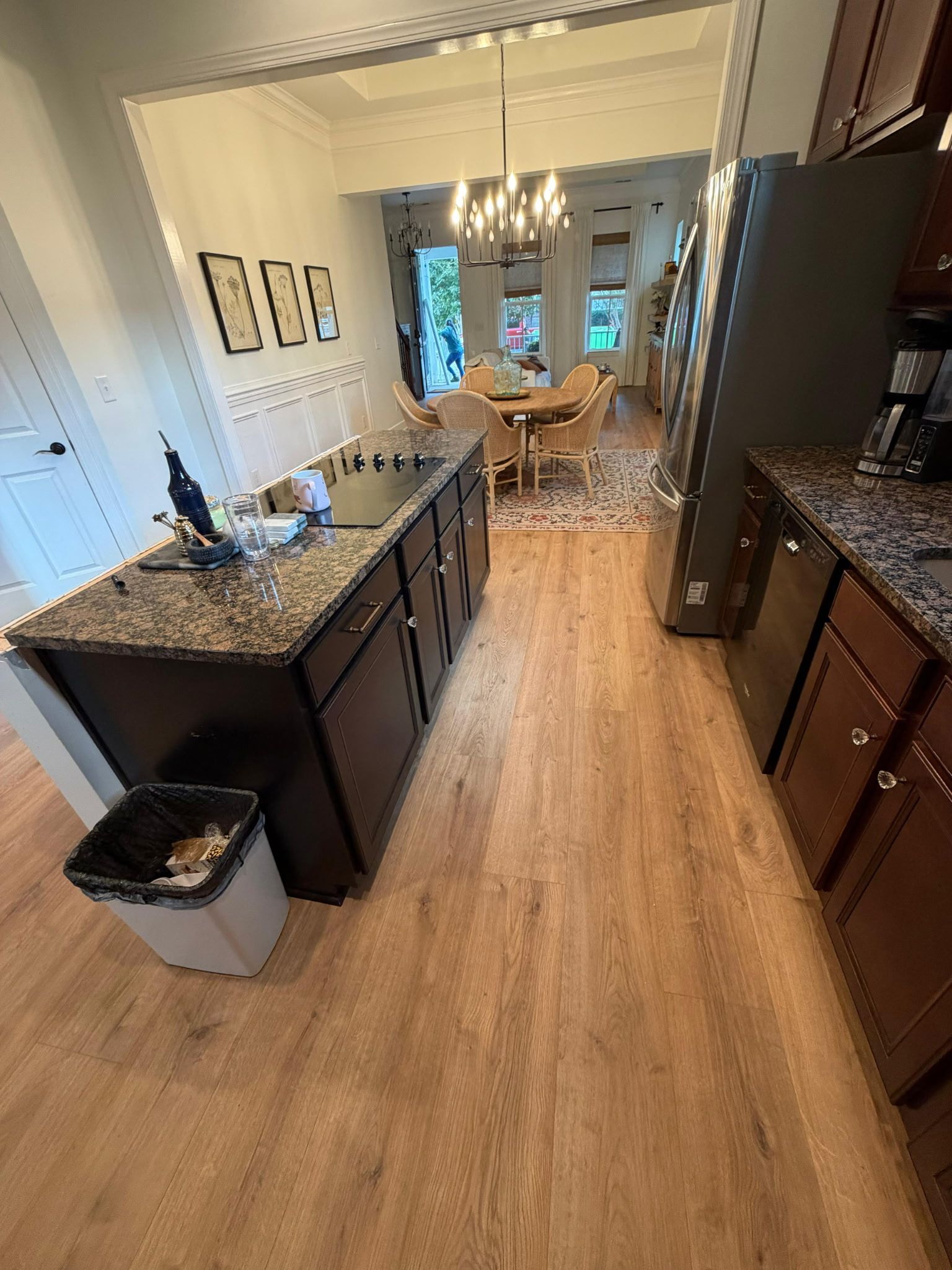 Kitchen with dark cabinets, granite counters, and light wood floors, leading to a dining area.