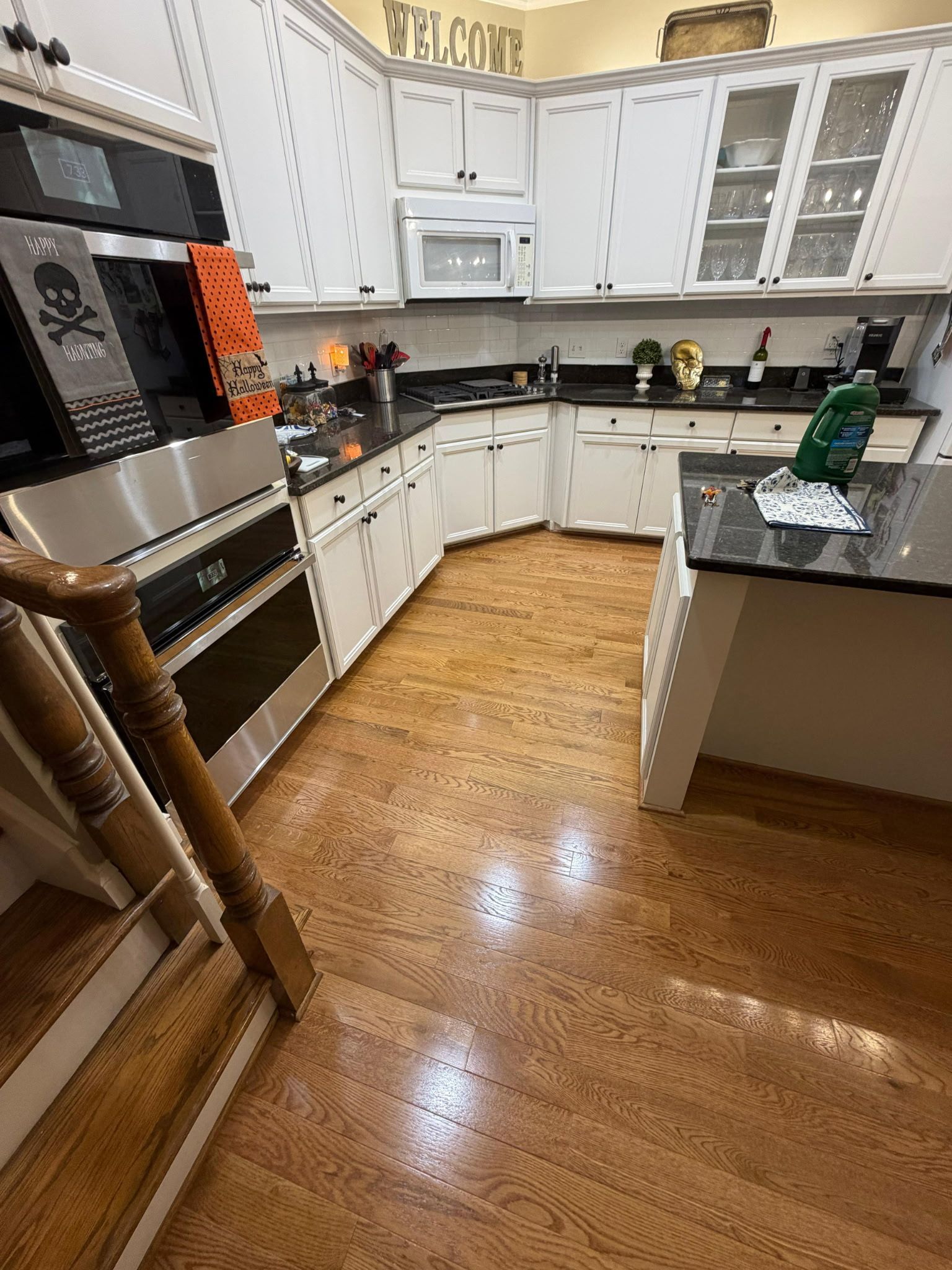 Bright kitchen with white cabinets, wood floors, black countertops, and stainless steel appliances.