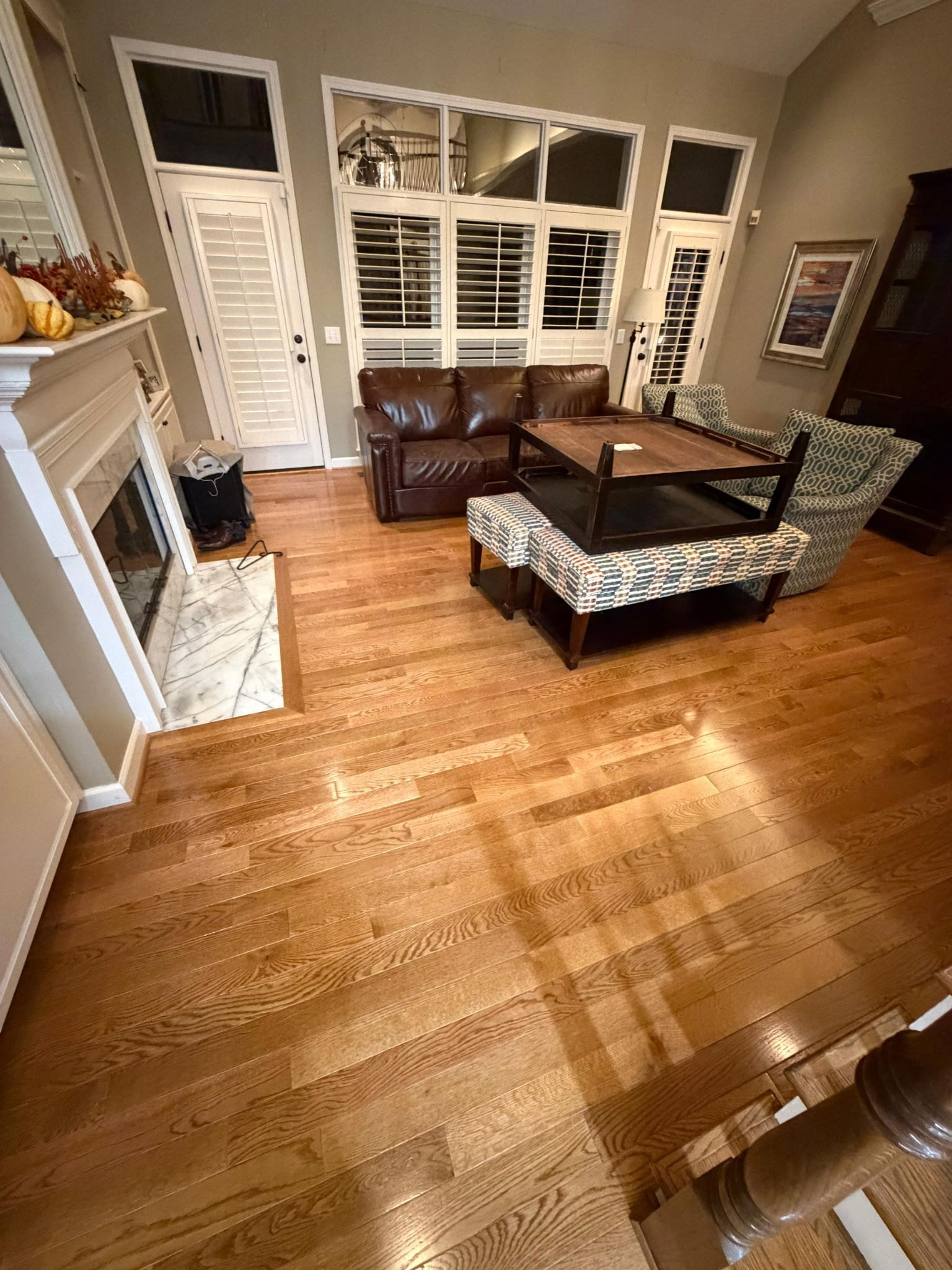 Living room with hardwood floors, white shutters, fireplace, and patterned sofa and chairs