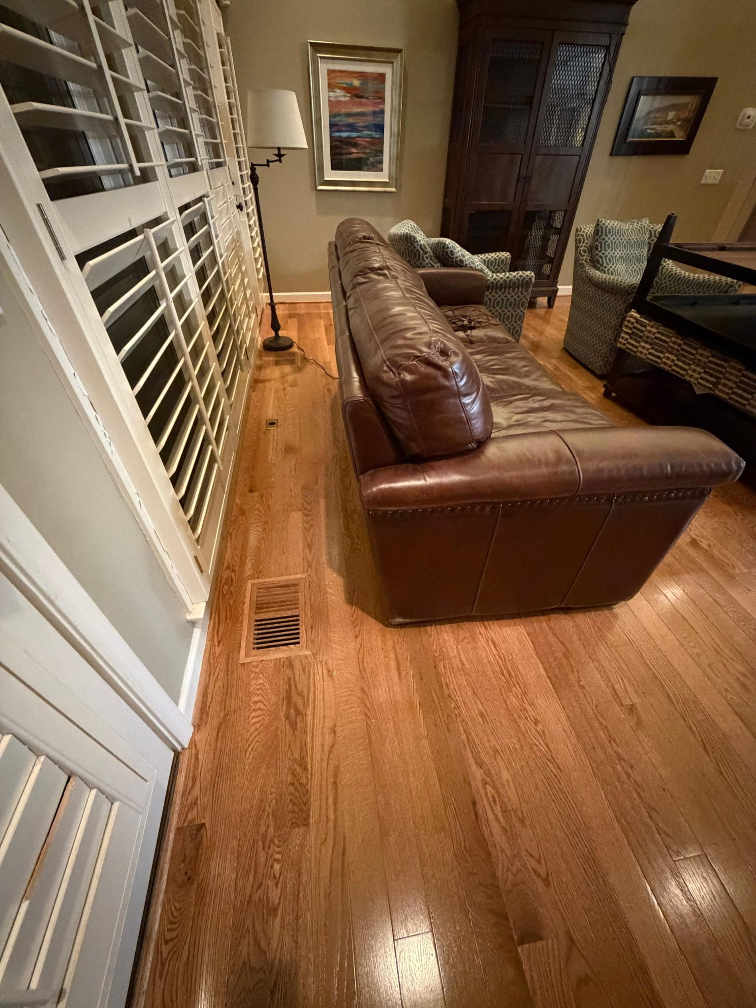 Living room with leather sofas, hardwood floor, and windows with white blinds.