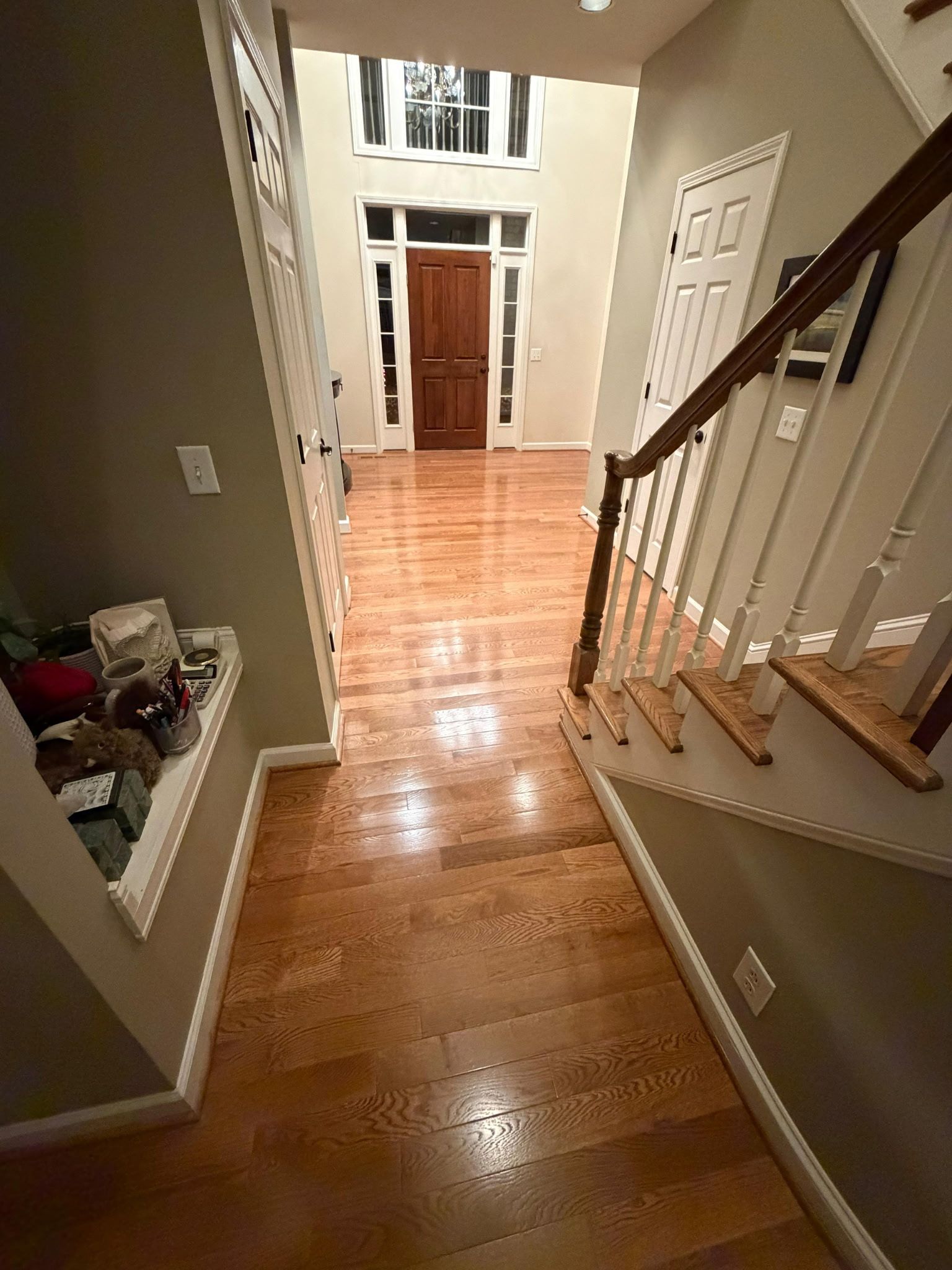 Stair landing with polished wood floor, white railings, and a hallway leading to front doors