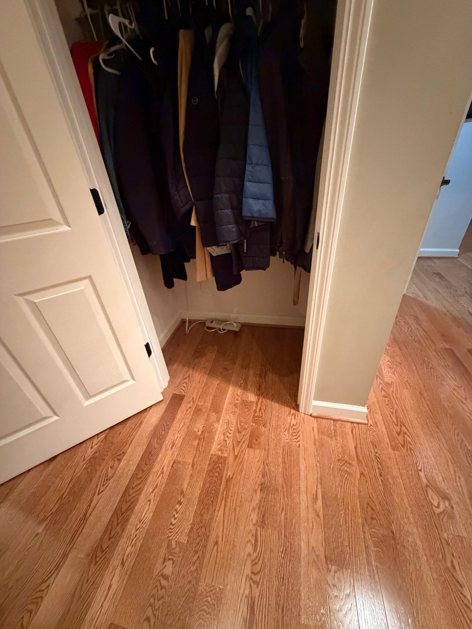 Open closet with hanging clothes and wooden floor in a hallway corner