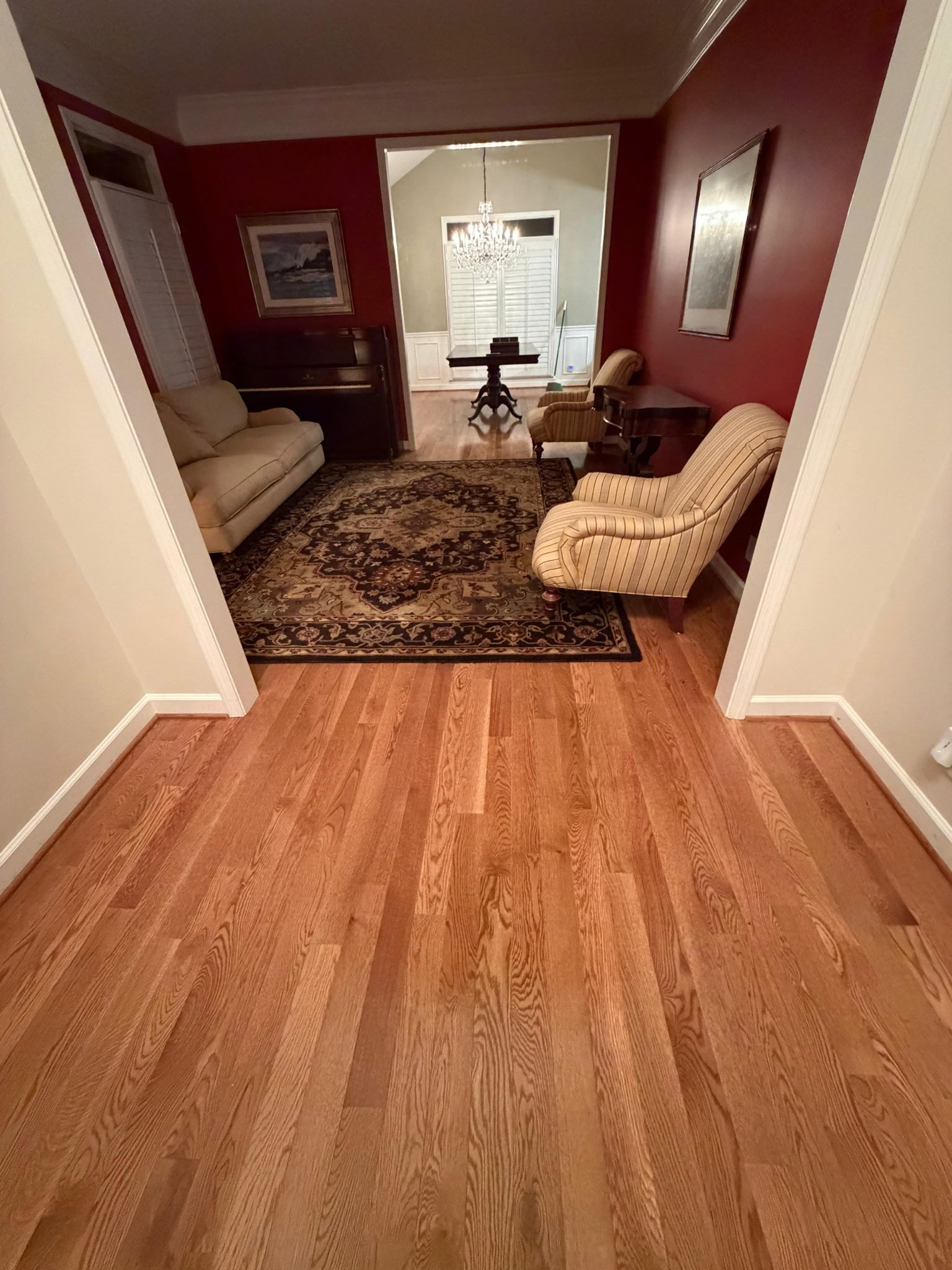 Hallway with hardwood floor, leading to a cozy living room with red walls, couches, and a patterned rug.