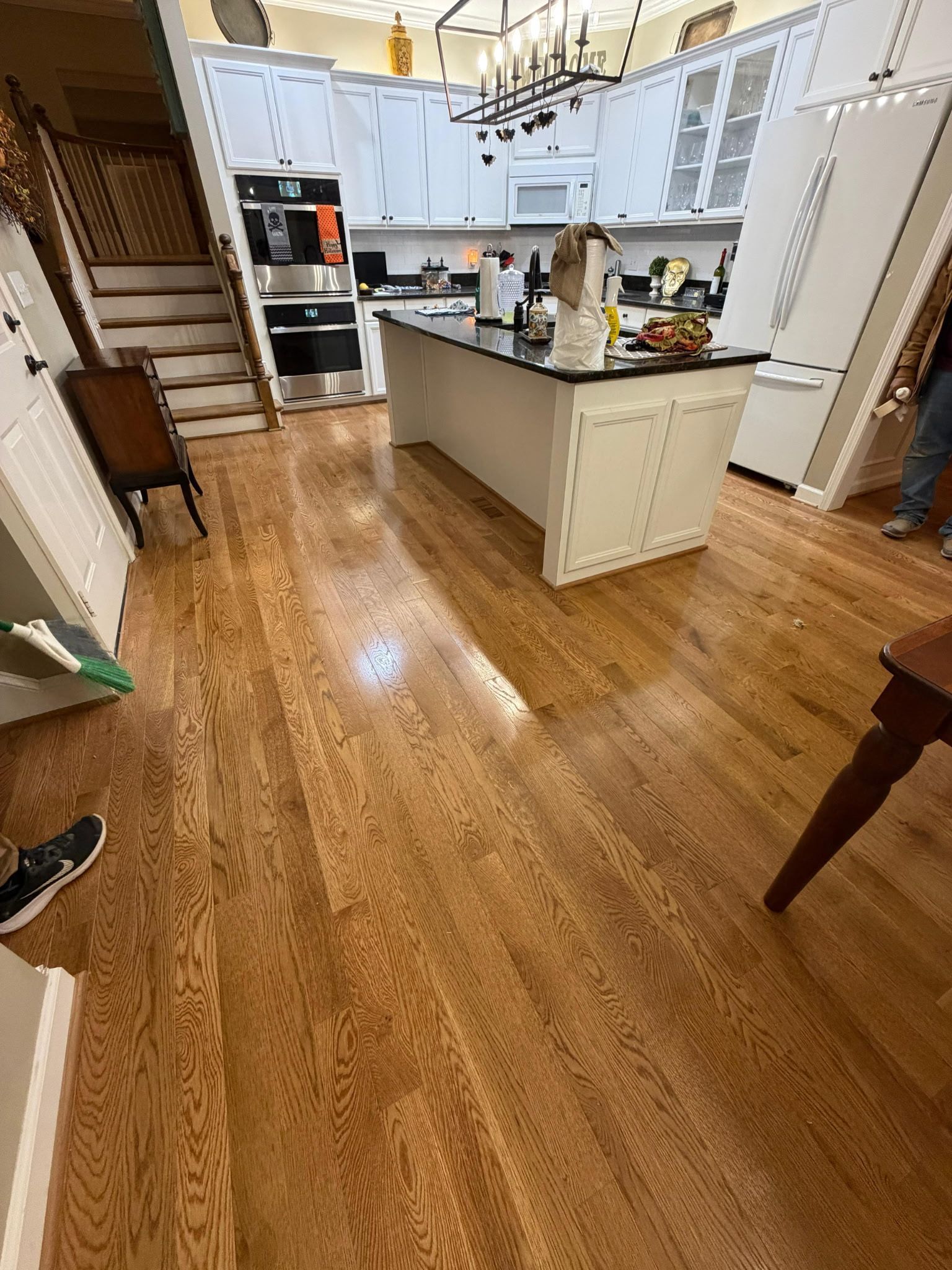 Bright kitchen with white cabinets, island, hardwood floors, and staircase in the background