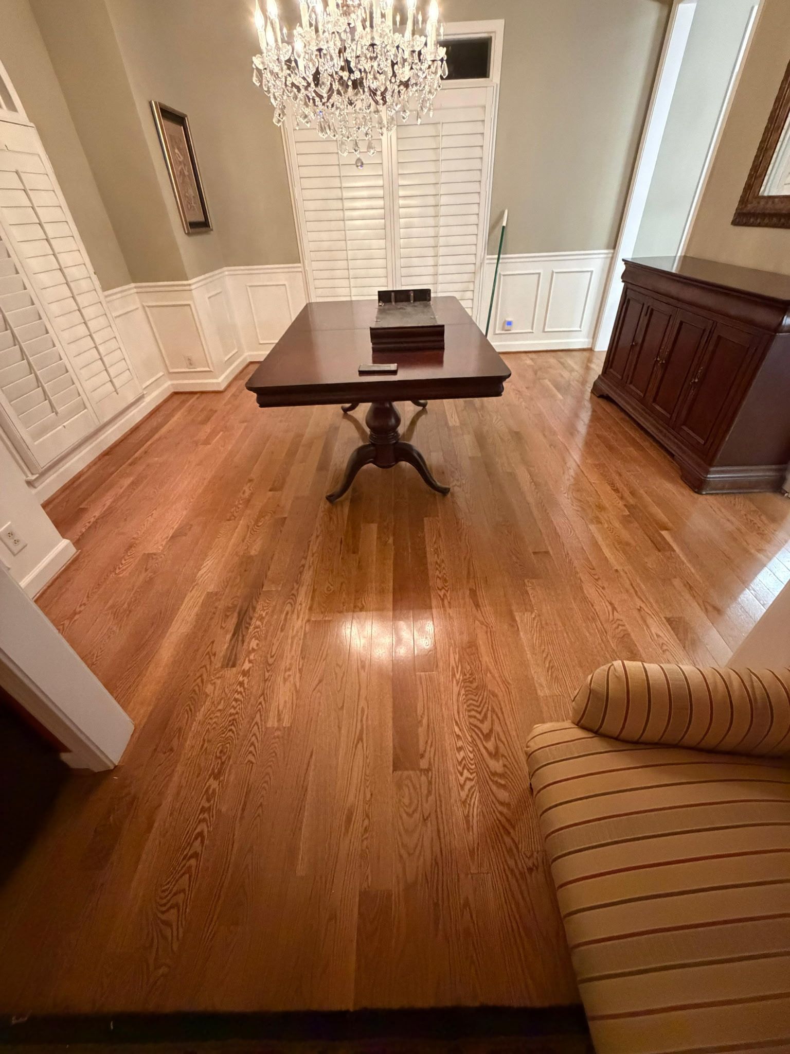 Dining room with hardwood floors, chandelier, white wainscoting, and a dark wooden table centered in the room.