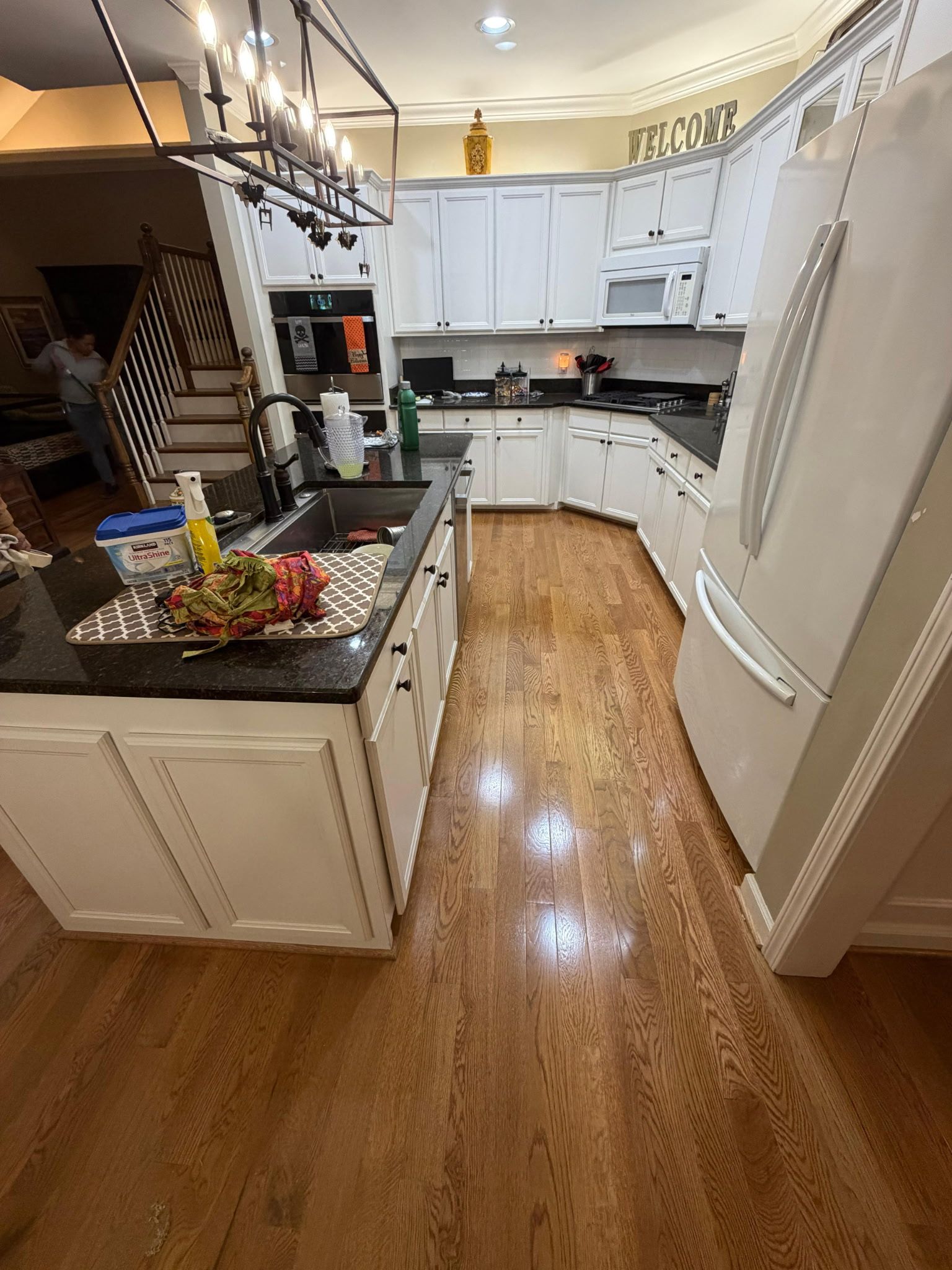 Bright kitchen with white cabinets, black countertops, wooden floor, and island under pendant lights.