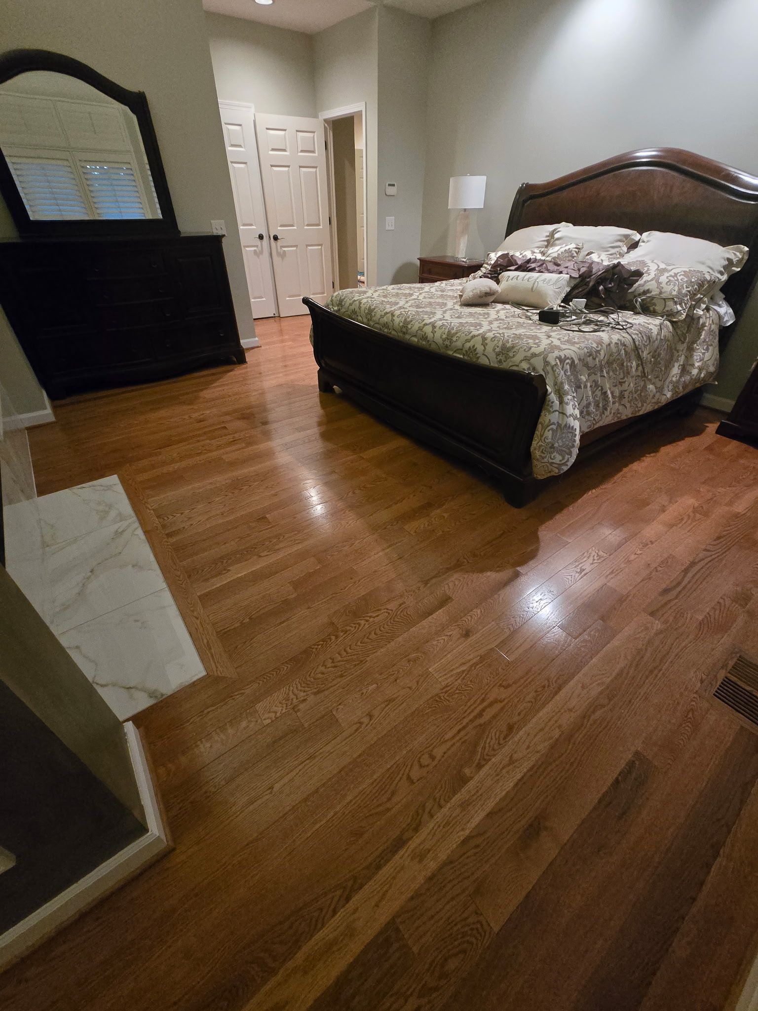 Bedroom with dark wood floor, queen bed, mirrored dresser, and open door in the background