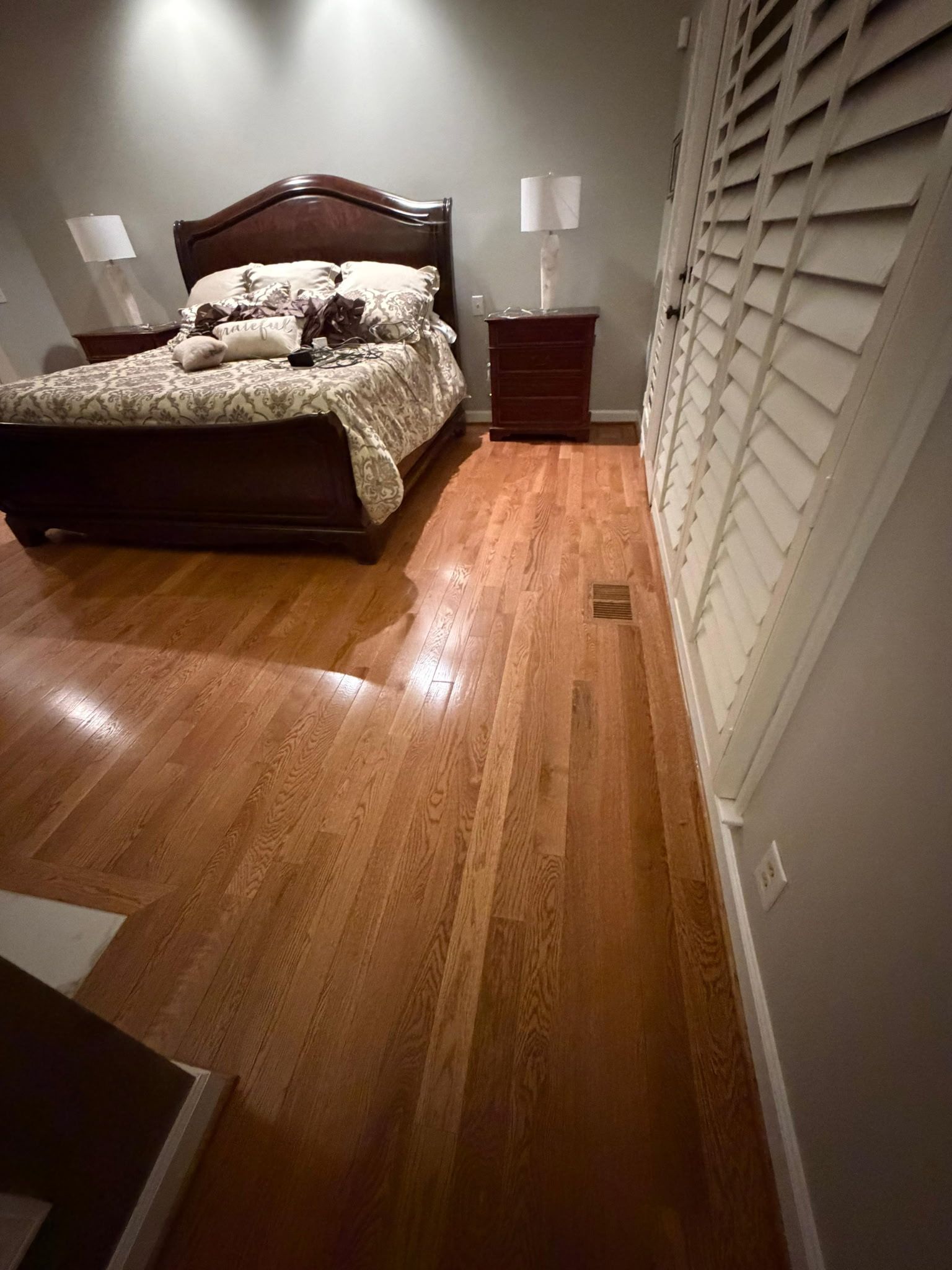 Bedroom with a dark wood bed, nightstands, lamps, and white shutters on a hardwood floor.