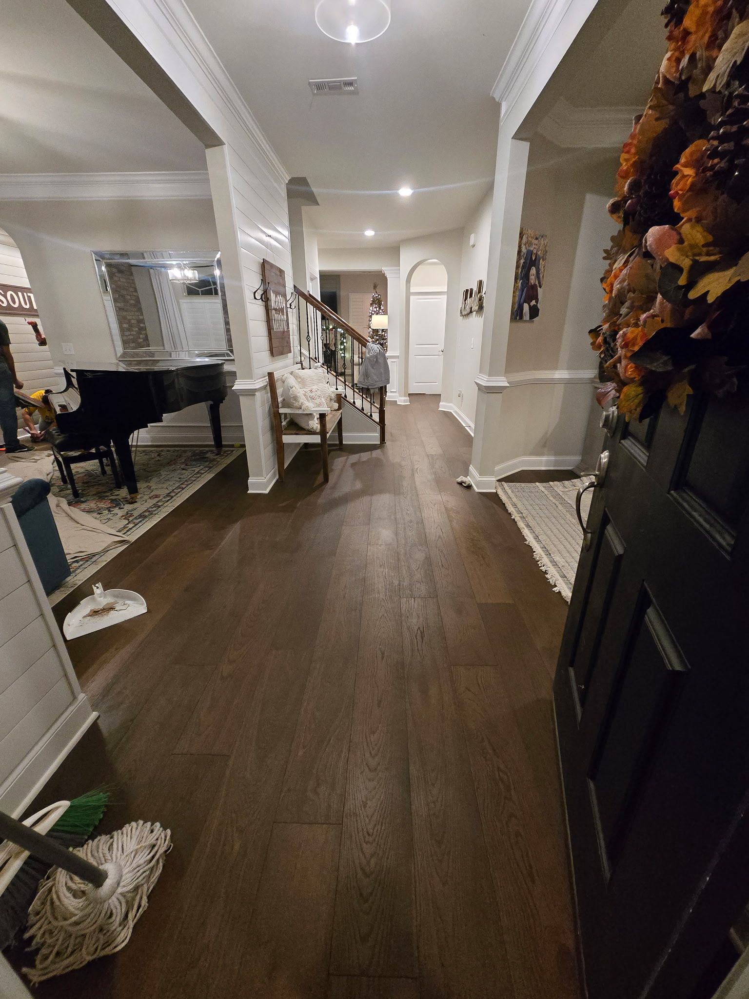 Bright hallway with dark wood floors, white columns, and a black grand piano in the adjacent room.