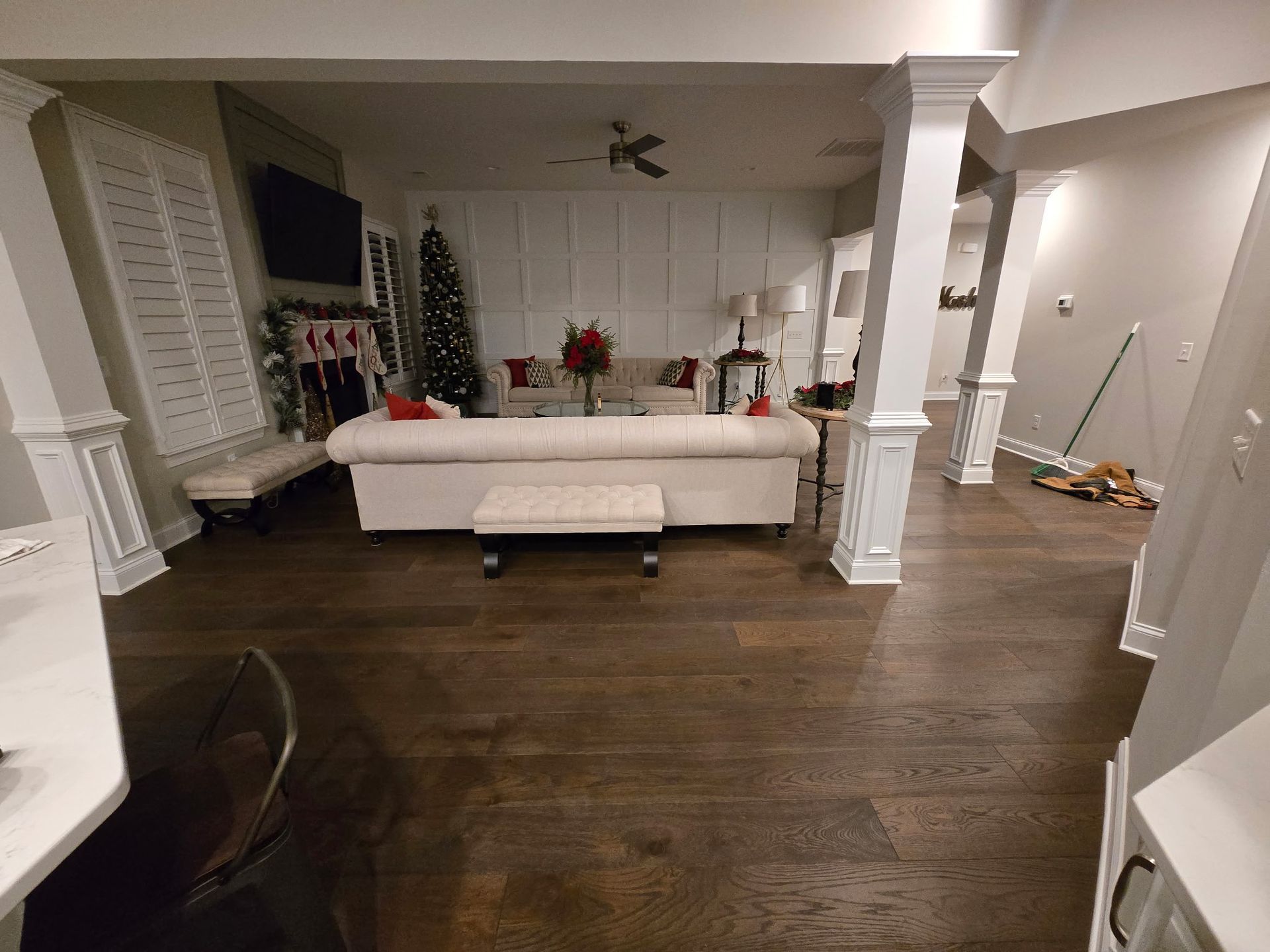 Spacious living room with dark wood floors, white sofa, TV, and Christmas decorations near a fireplace.