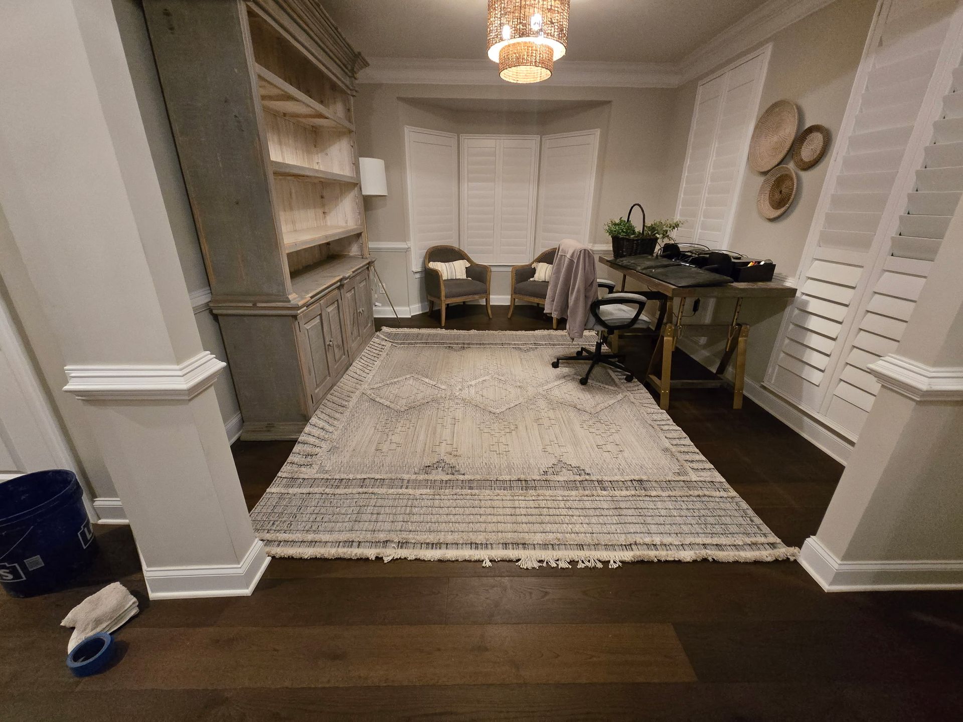 Open dining room with rug, chandelier, white shutters, and a desk along the back wall.