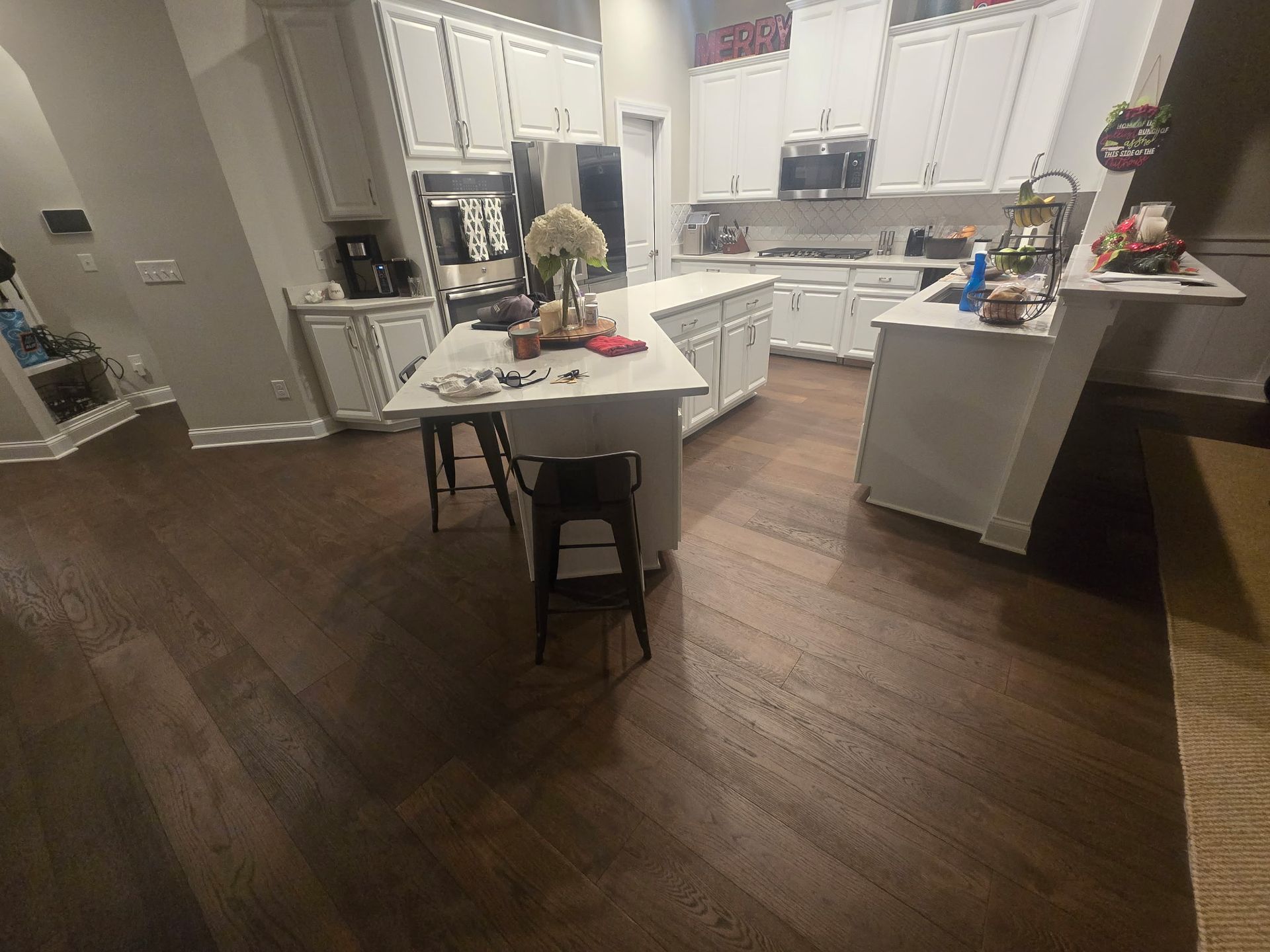 Modern kitchen with white cabinets, island table, and dark wood floors, viewed from the dining area