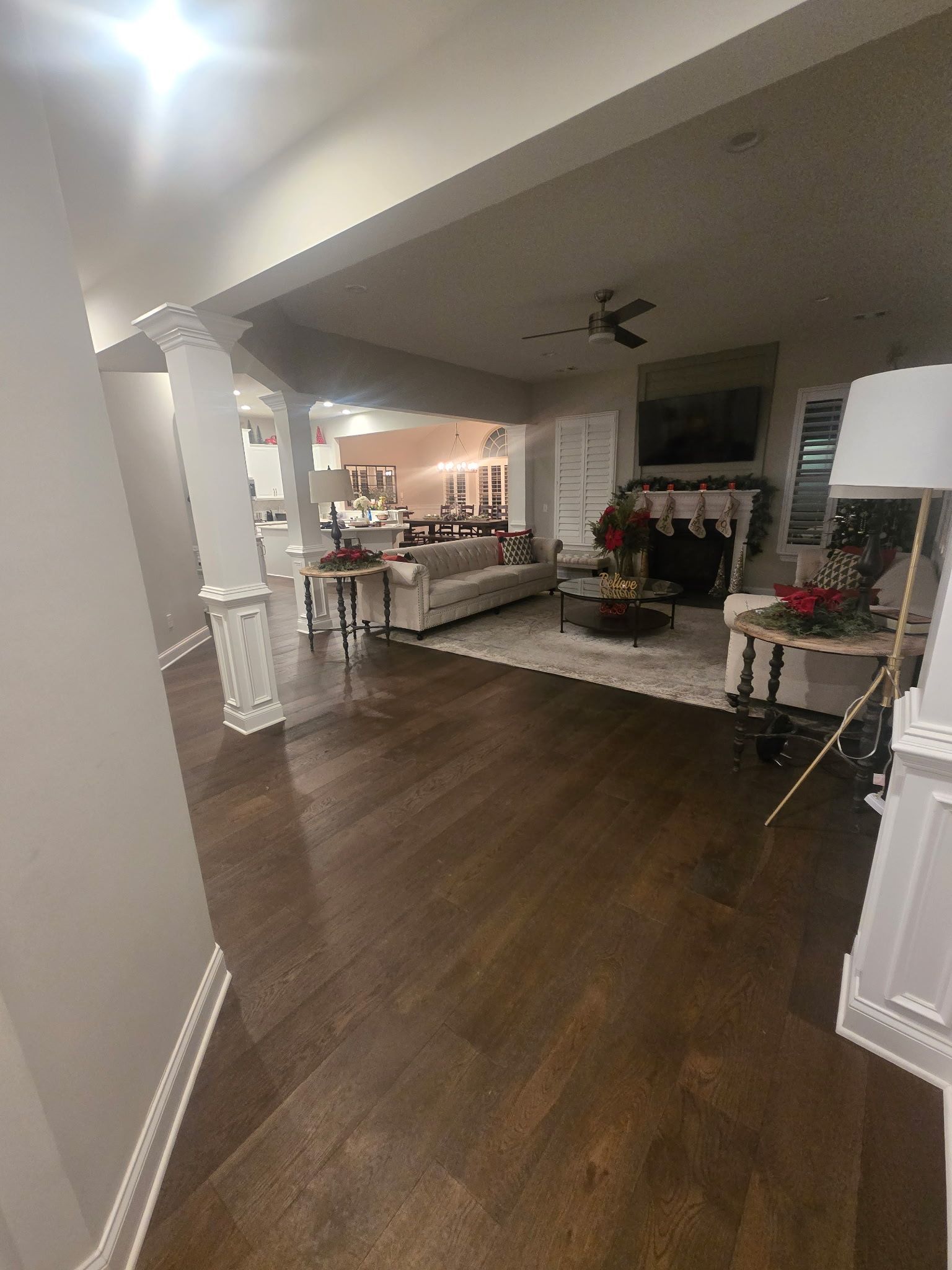 Spacious dining room with dark wood floors, white columns, and a decorated table in the background