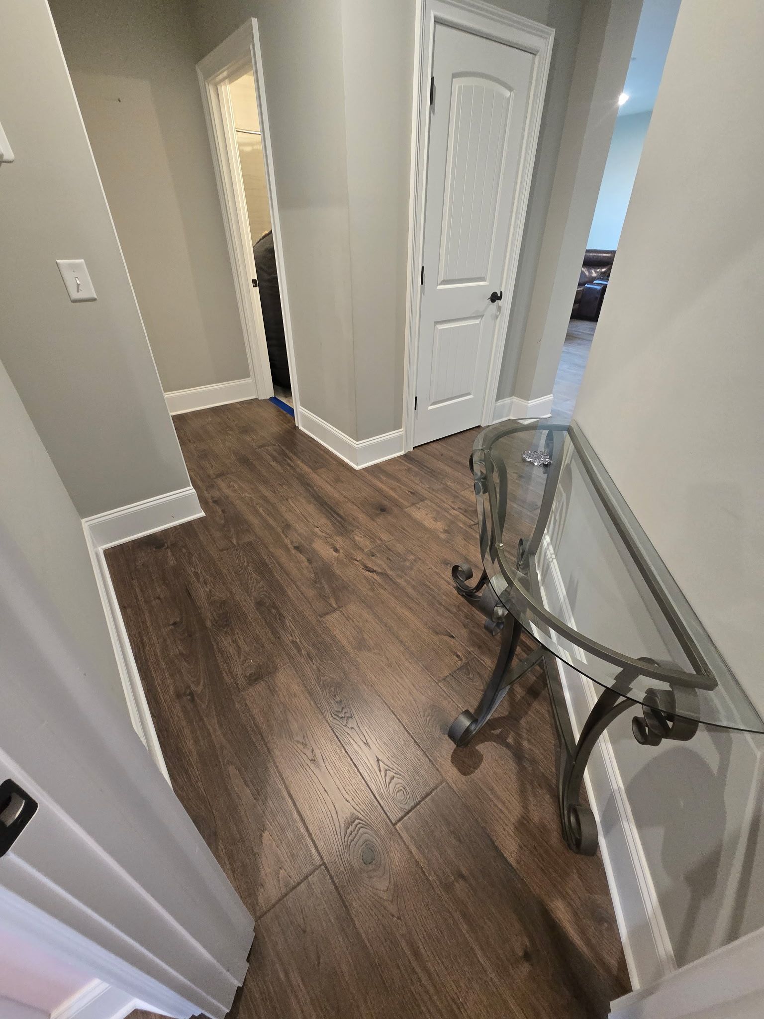 Hallway with wood flooring, white doors, and a glass-and-metal table by the wall.