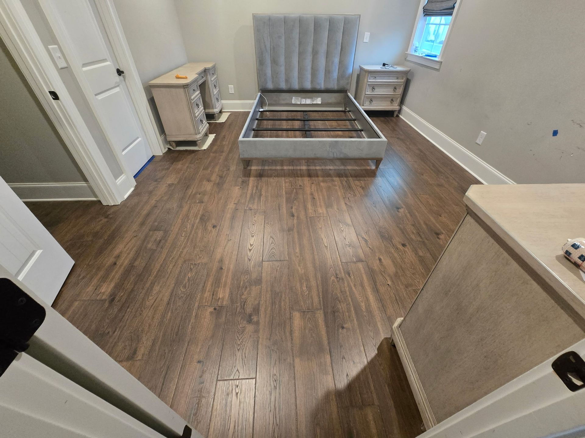 Empty bedroom with hardwood floor, bed frame, and gray curtains by a window.