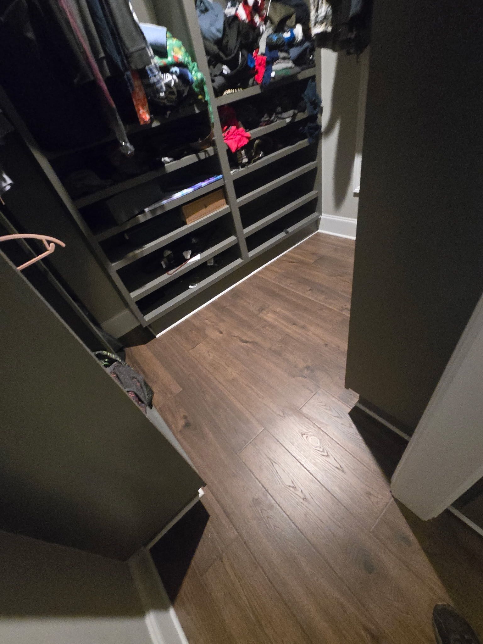Walk-in closet with open shelving, hanging clothes, and wood flooring seen from the doorway