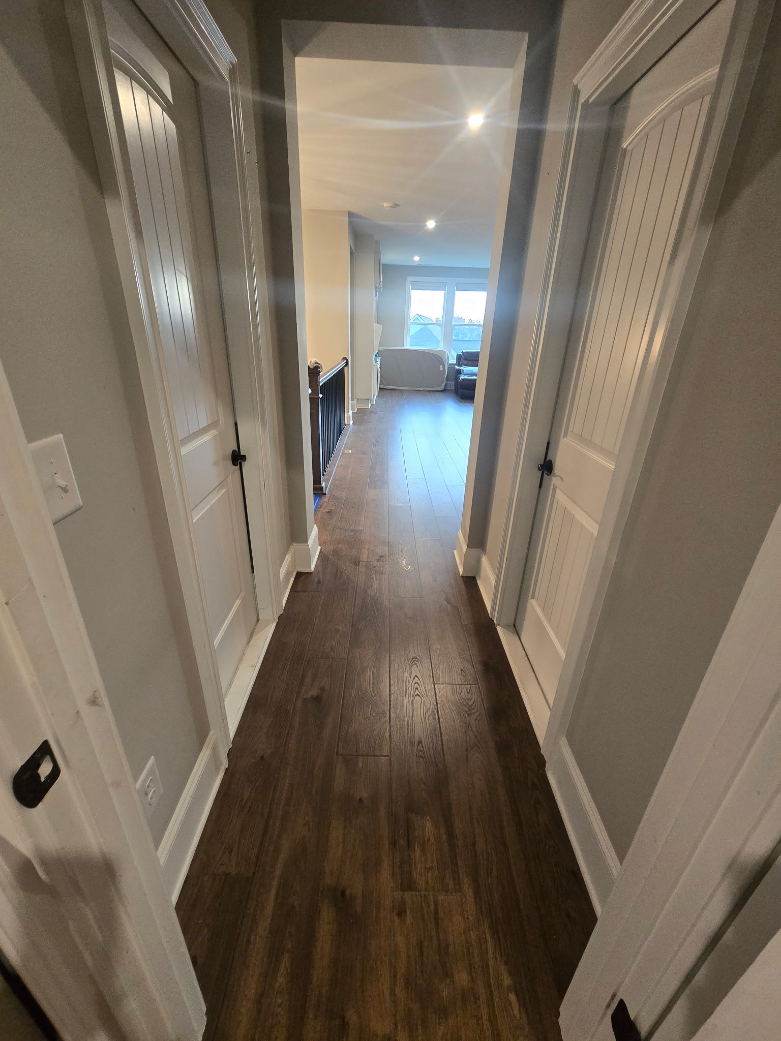 Narrow hallway with dark wood floors, white walls, and a bright room visible at the far end.