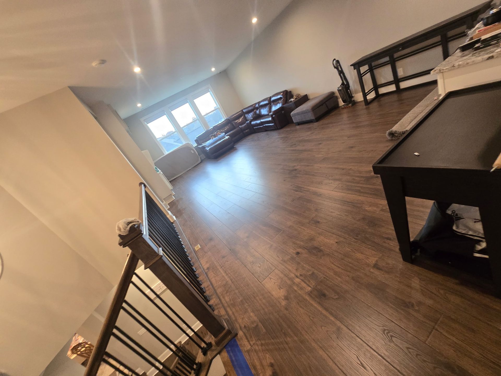 Spacious empty living room with wood floors, ceiling lights, and a pool table near a staircase