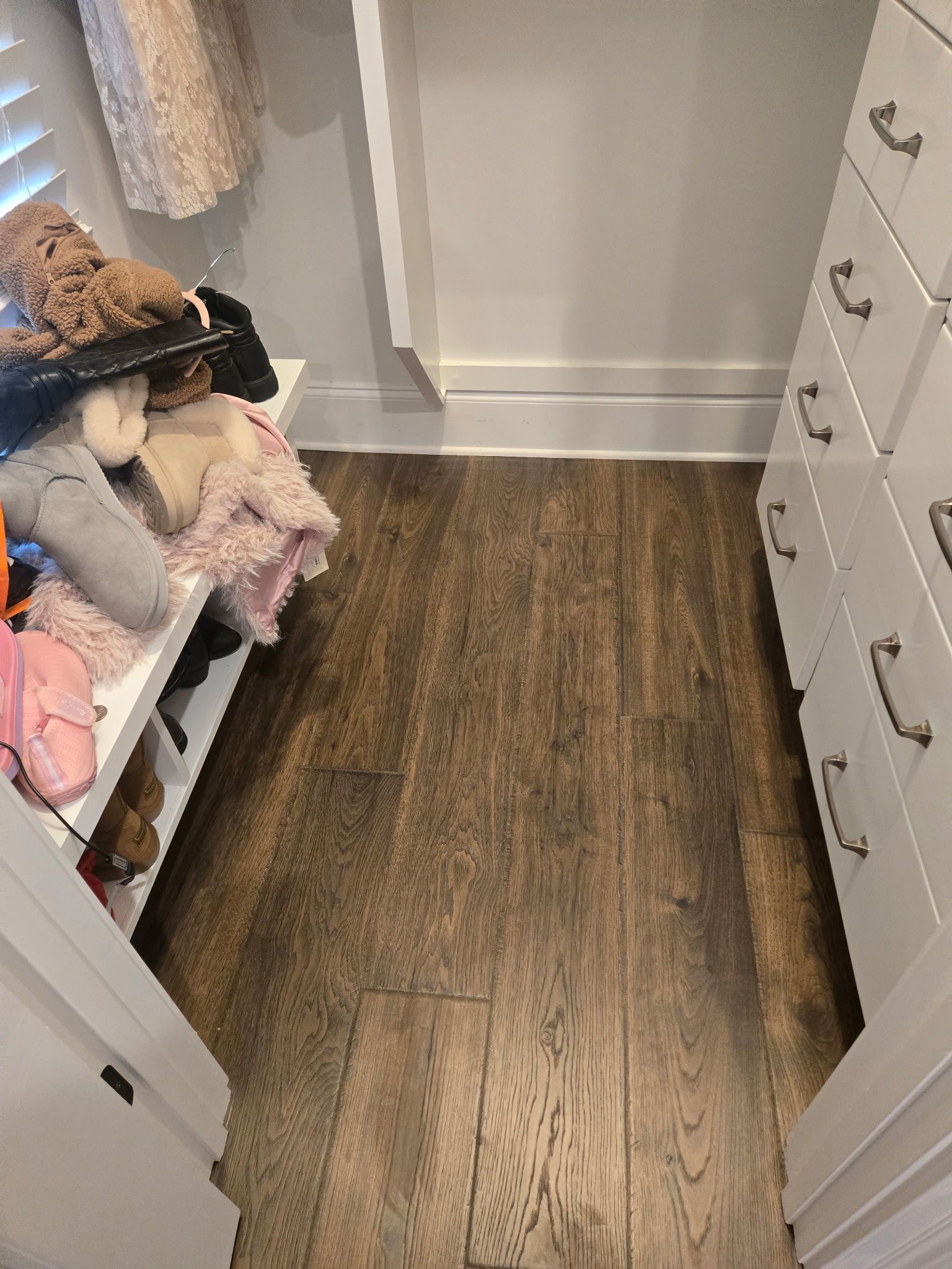Narrow closet with wood floor, hanging clothes on the left, and a white dresser on the right.