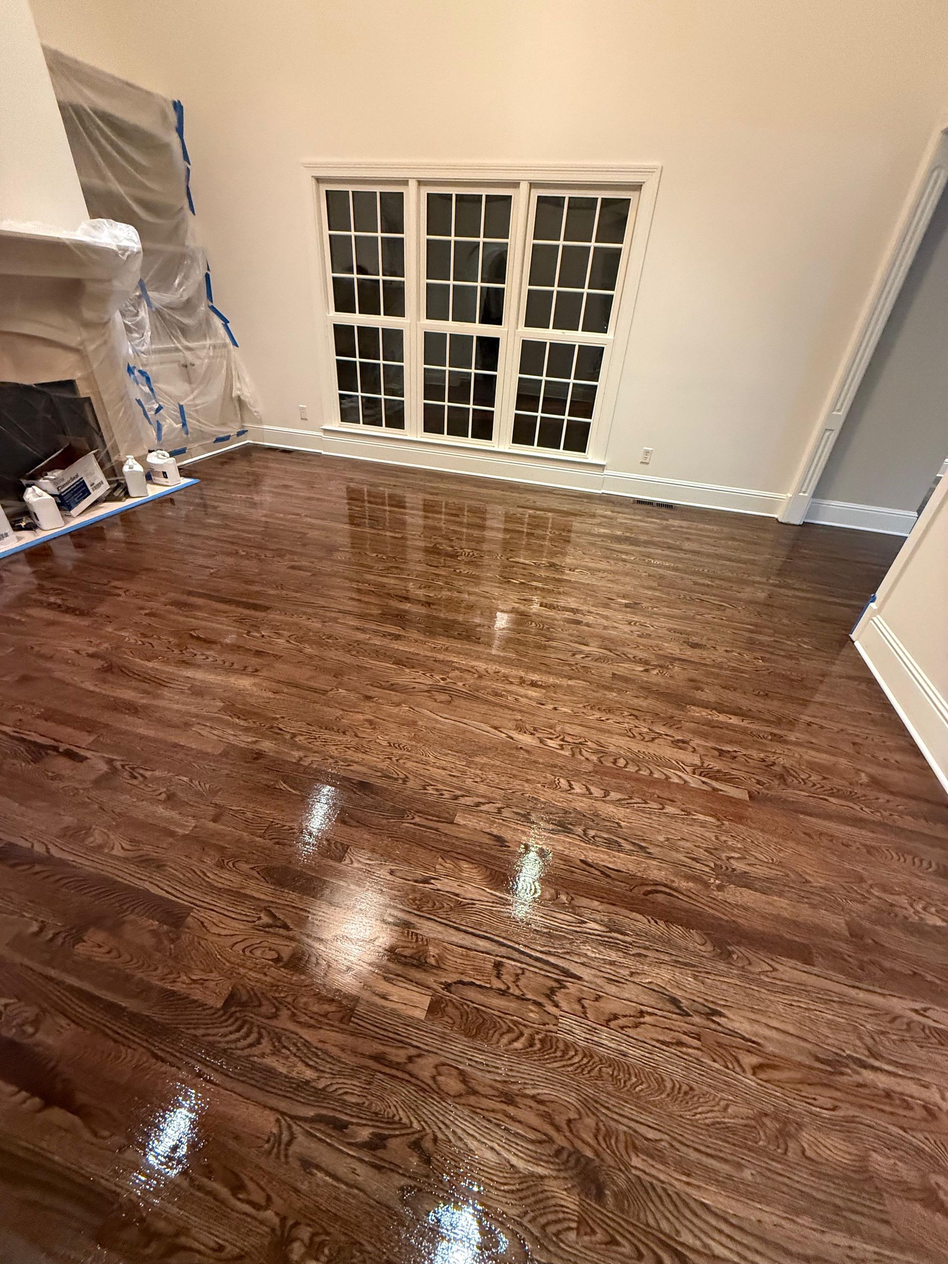 Empty room with glossy hardwood floor, window, and built-in shelving on the left.