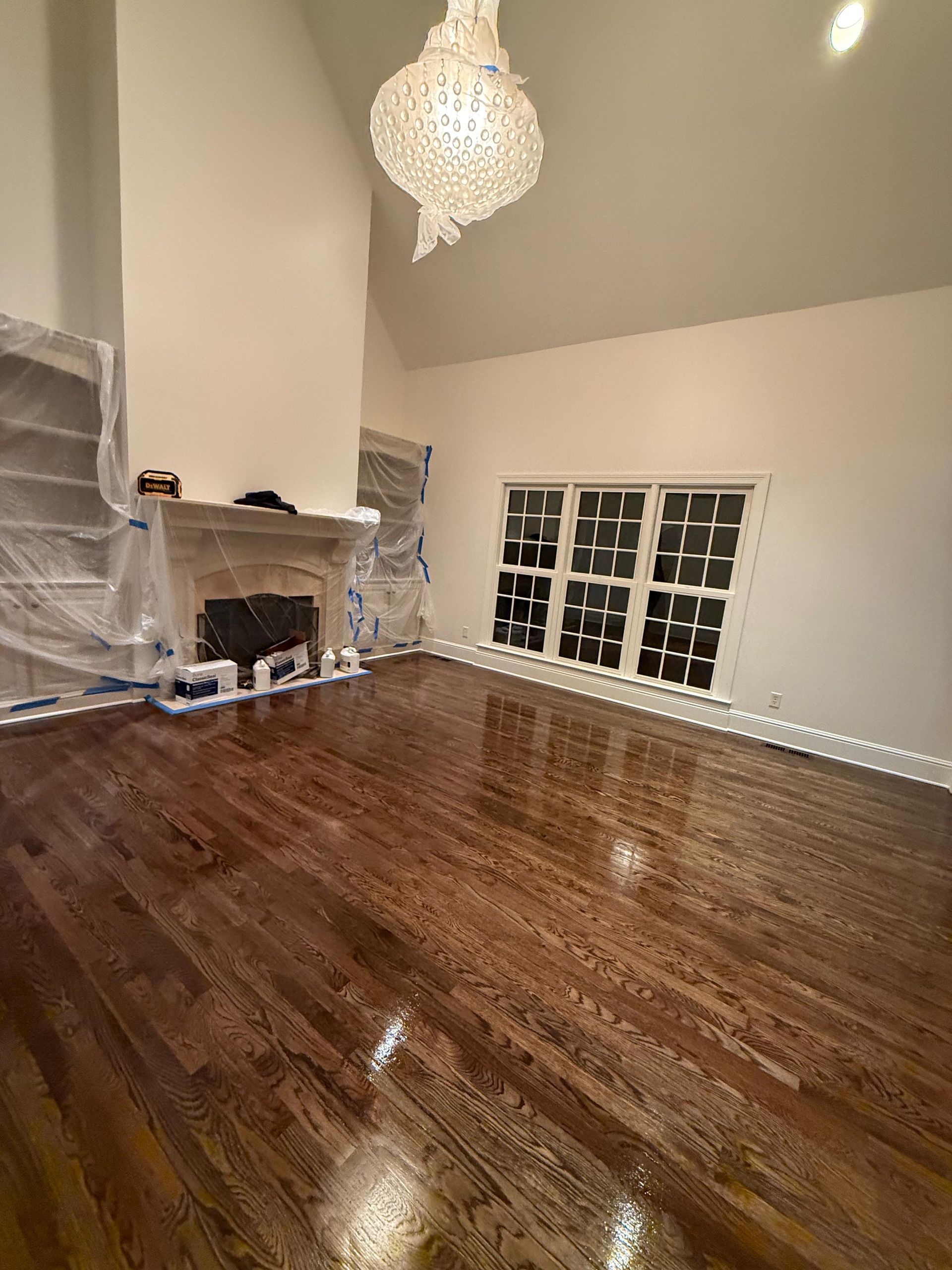 Empty living room with dark wood floors, chandelier, fireplace, and French doors leading outside