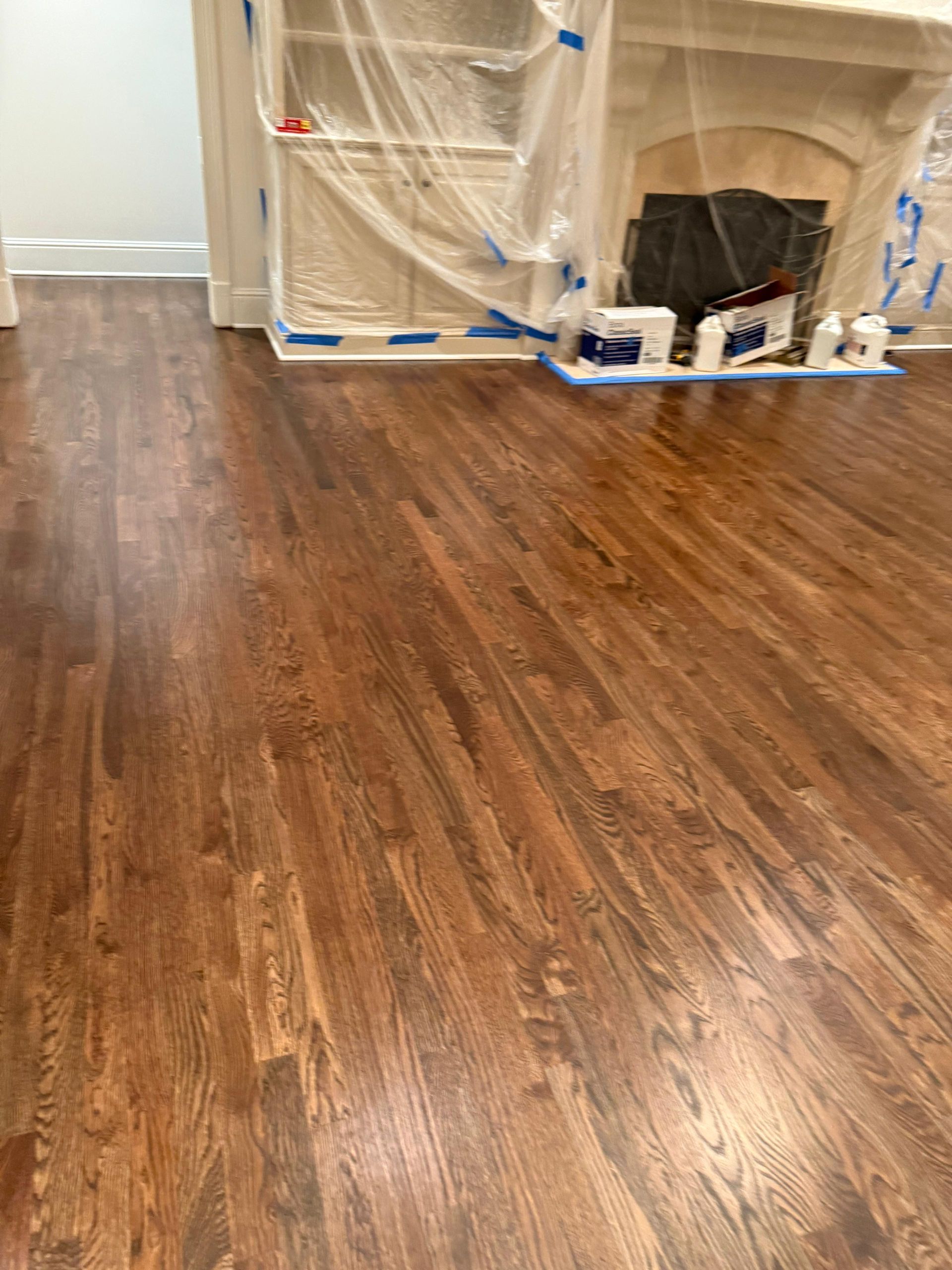 Hardwood floor with a fireplace area covered in plastic and painter’s tape during renovation