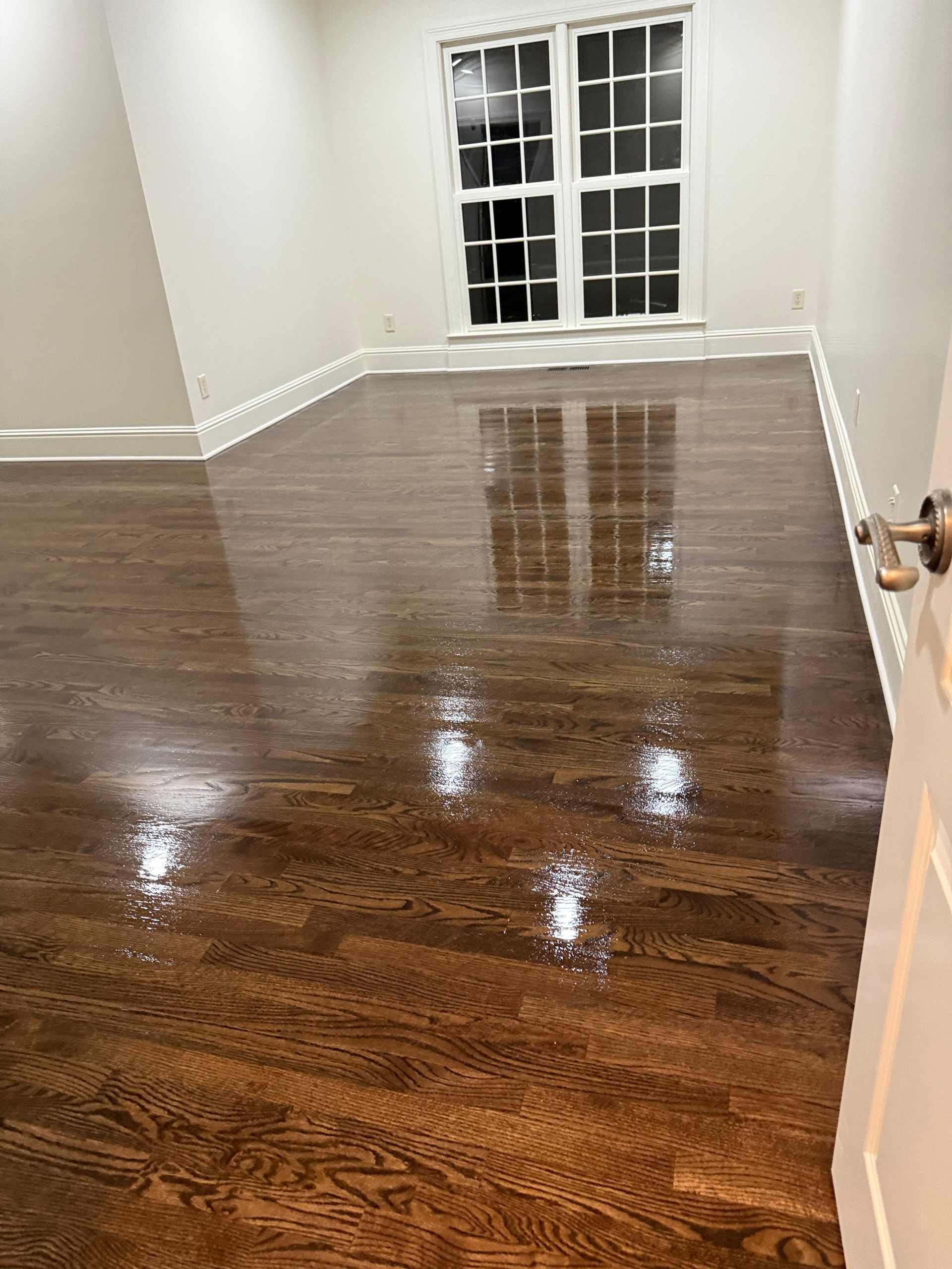 Empty room with glossy dark hardwood floors and white walls, viewed toward a French door.