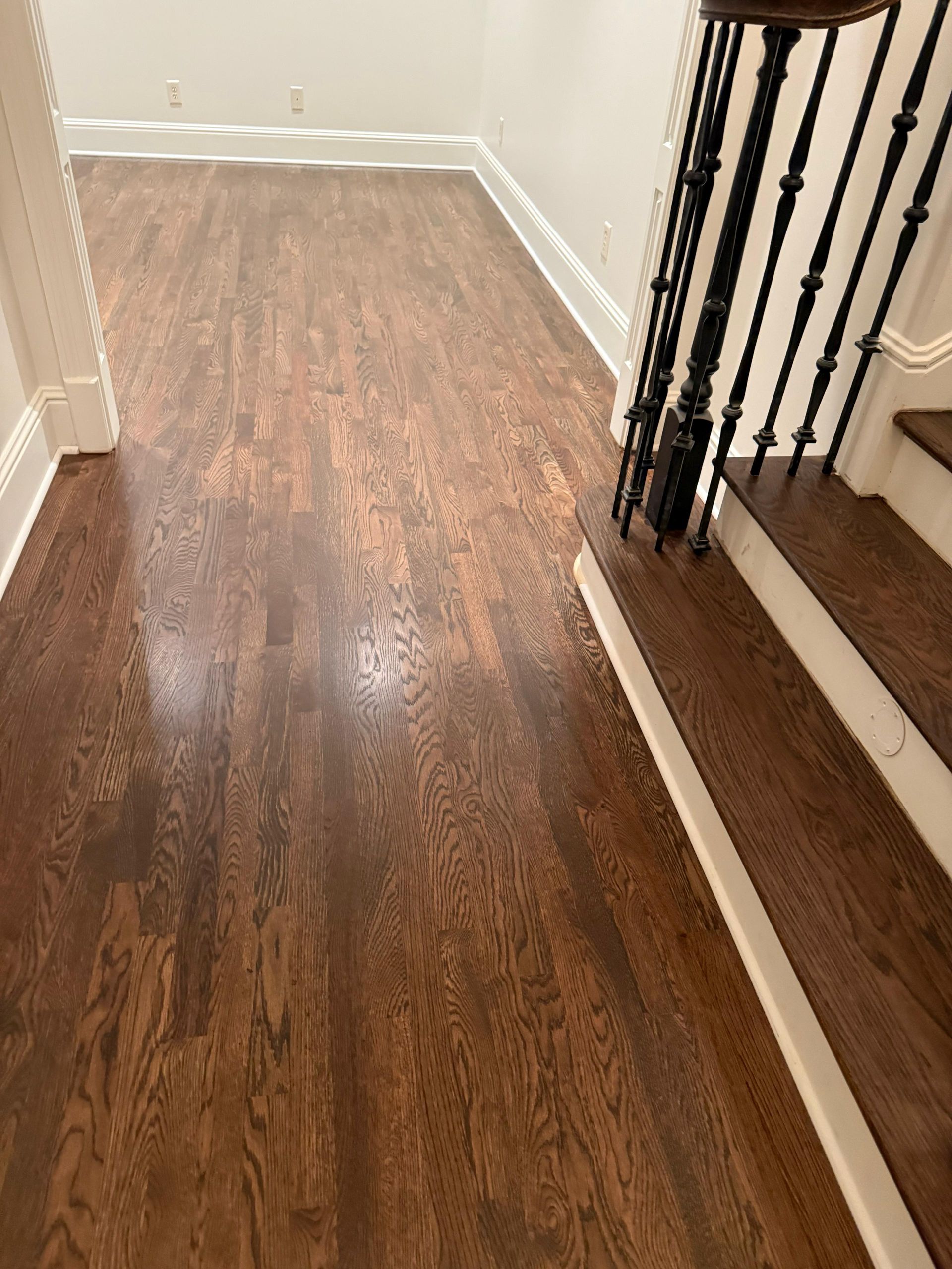 Wooden hallway floor leading to a staircase with black balusters and white trim
