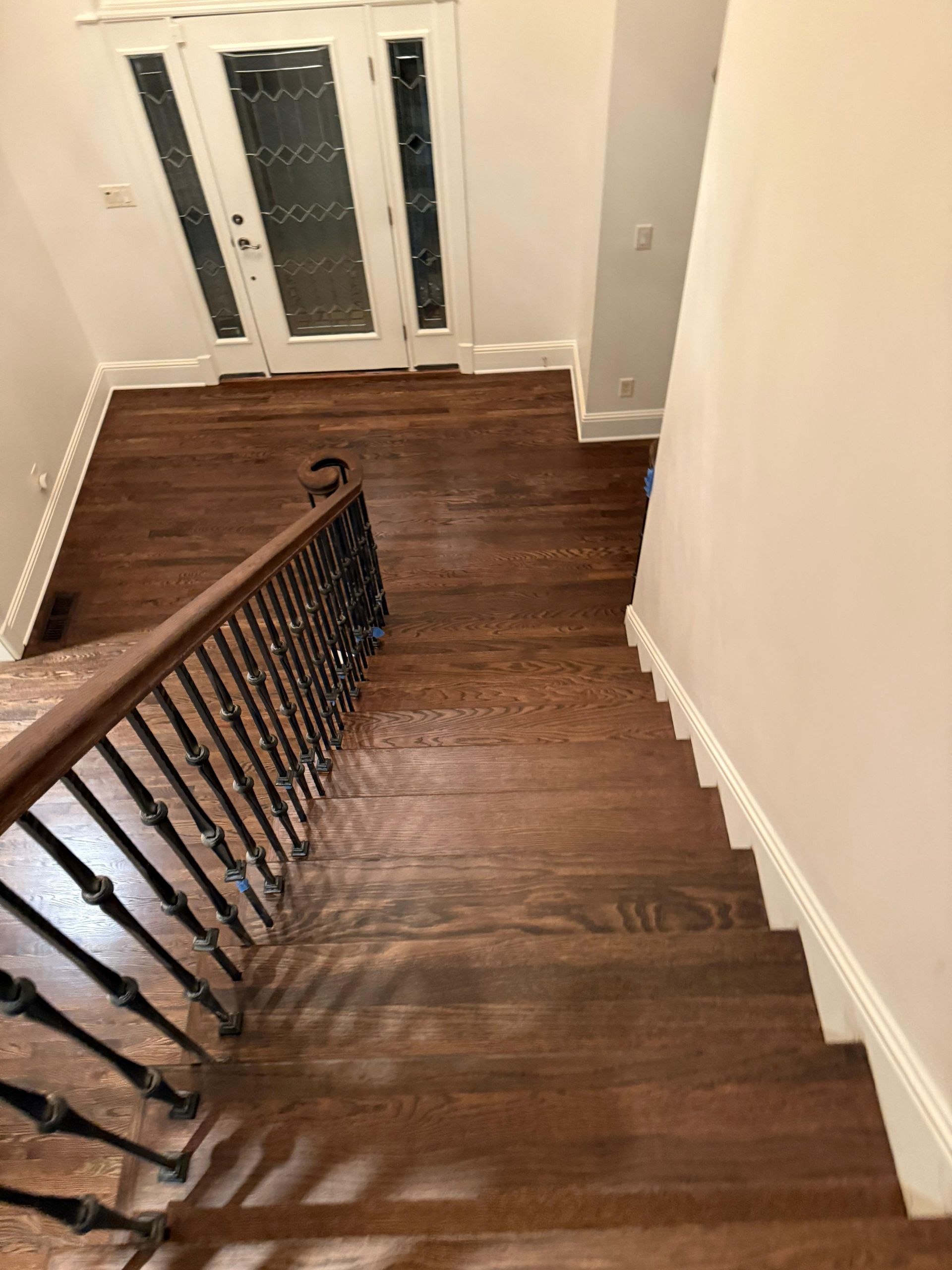Staircase with dark wood steps and black railing leading down to a white entry hall with double glass doors