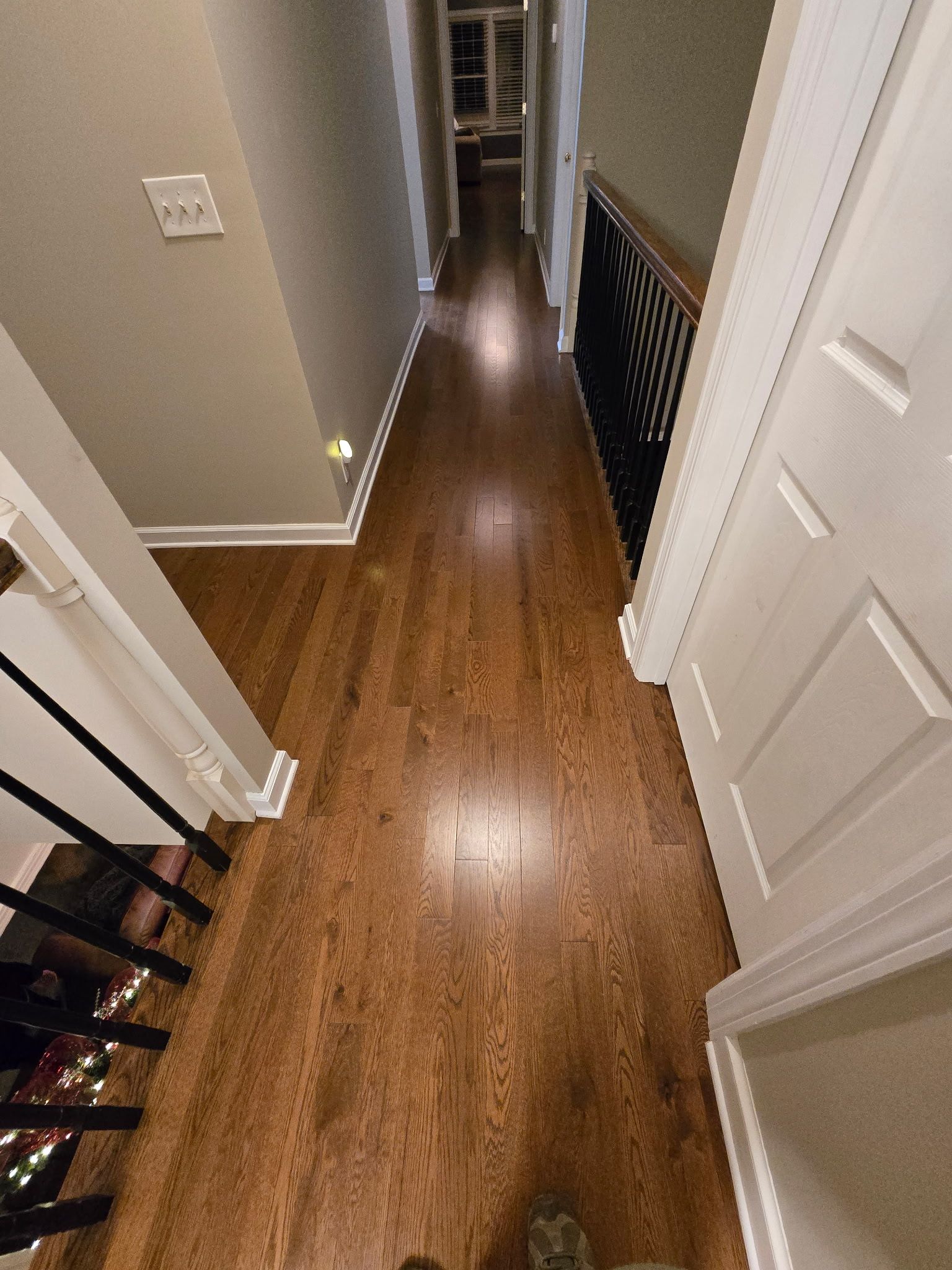 Narrow hallway with wood floor, beige walls, white doors, and a railing overlooking stairs.
