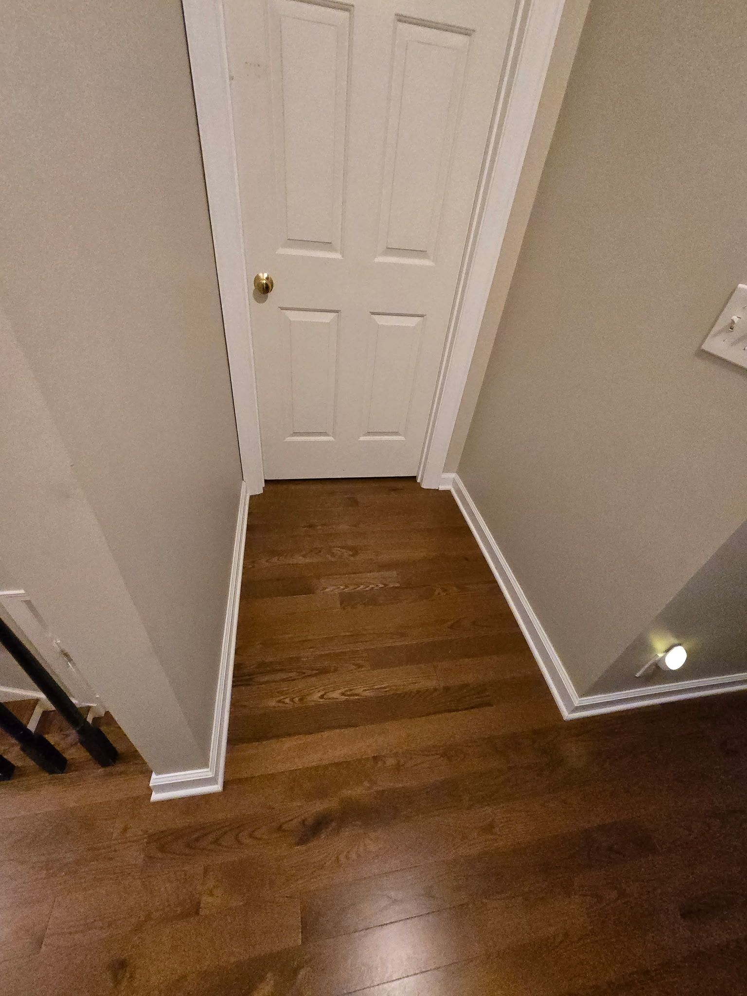 Narrow hallway with wood floor, white door, and beige walls.
