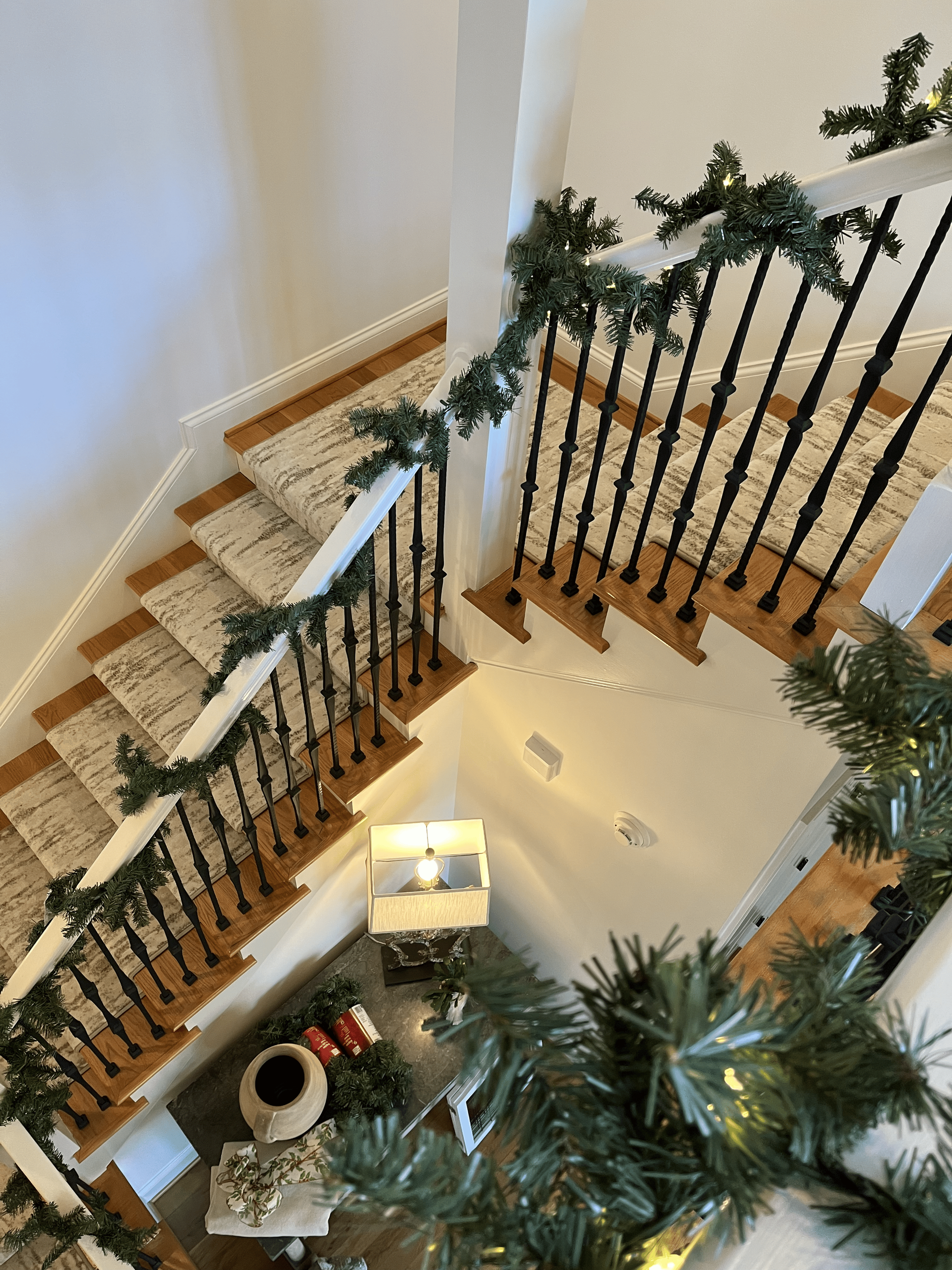 Staircase with black railings, beige carpet, and green garland in a bright home interior.