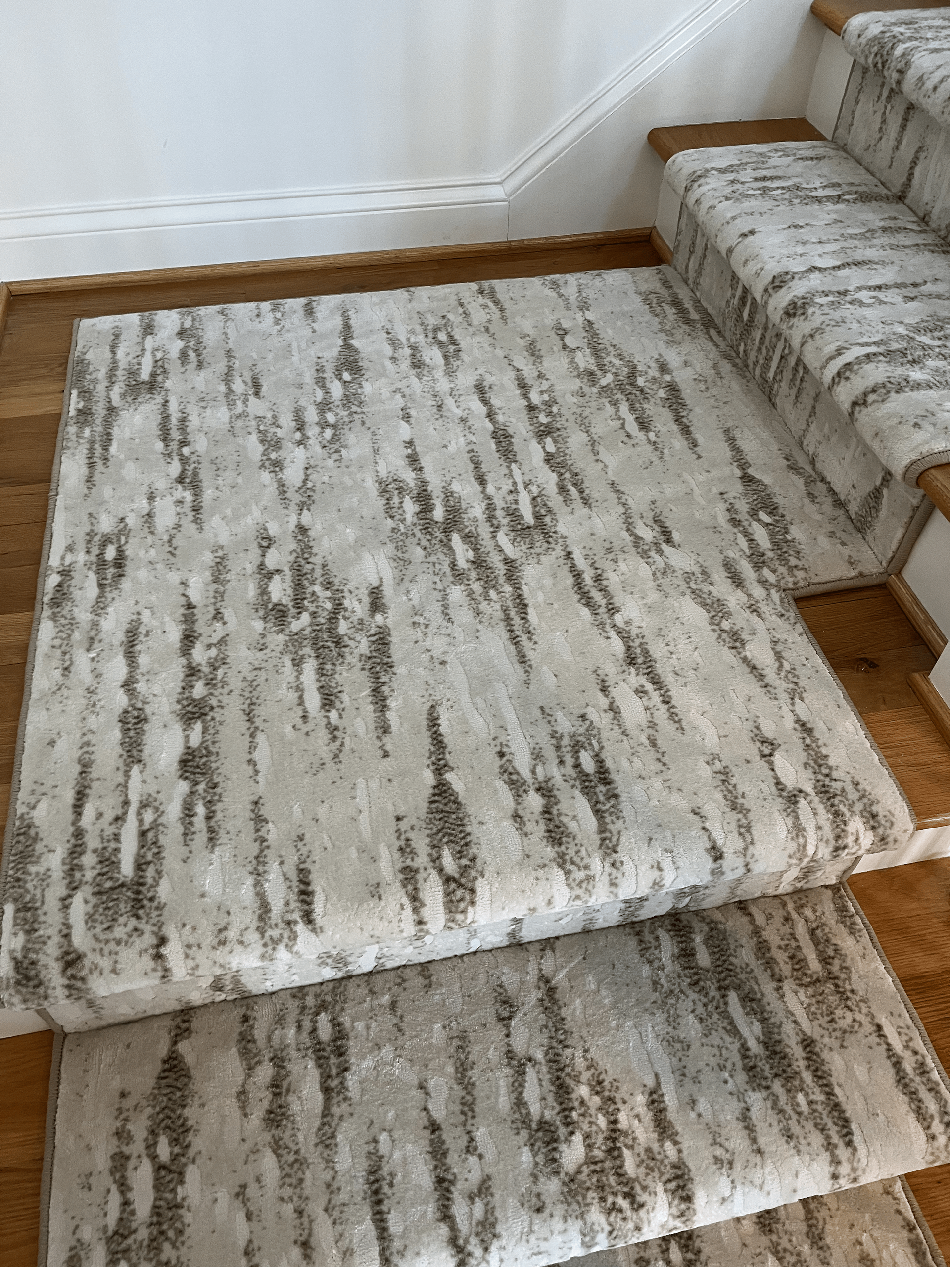 Staircase with a gray patterned runner carpet on wooden steps beside a striped upholstered sofa.