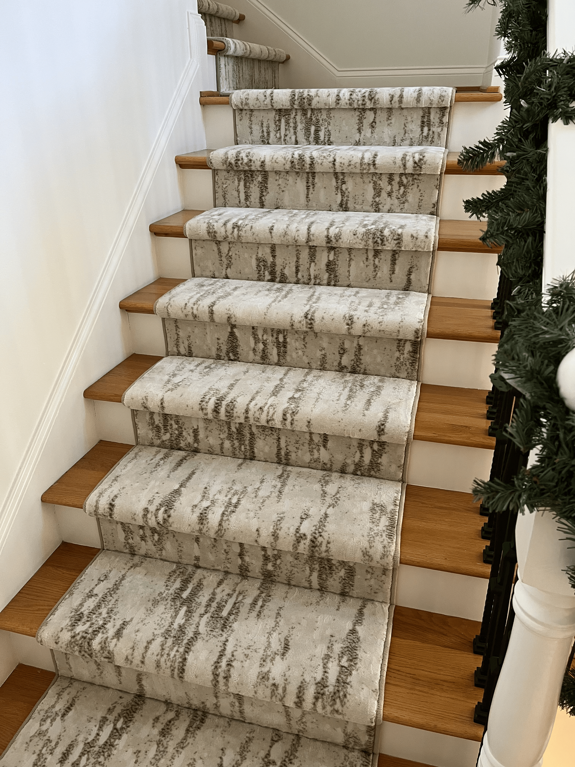 Carpeted staircase with white banister, tan steps, and holiday garland on the right side