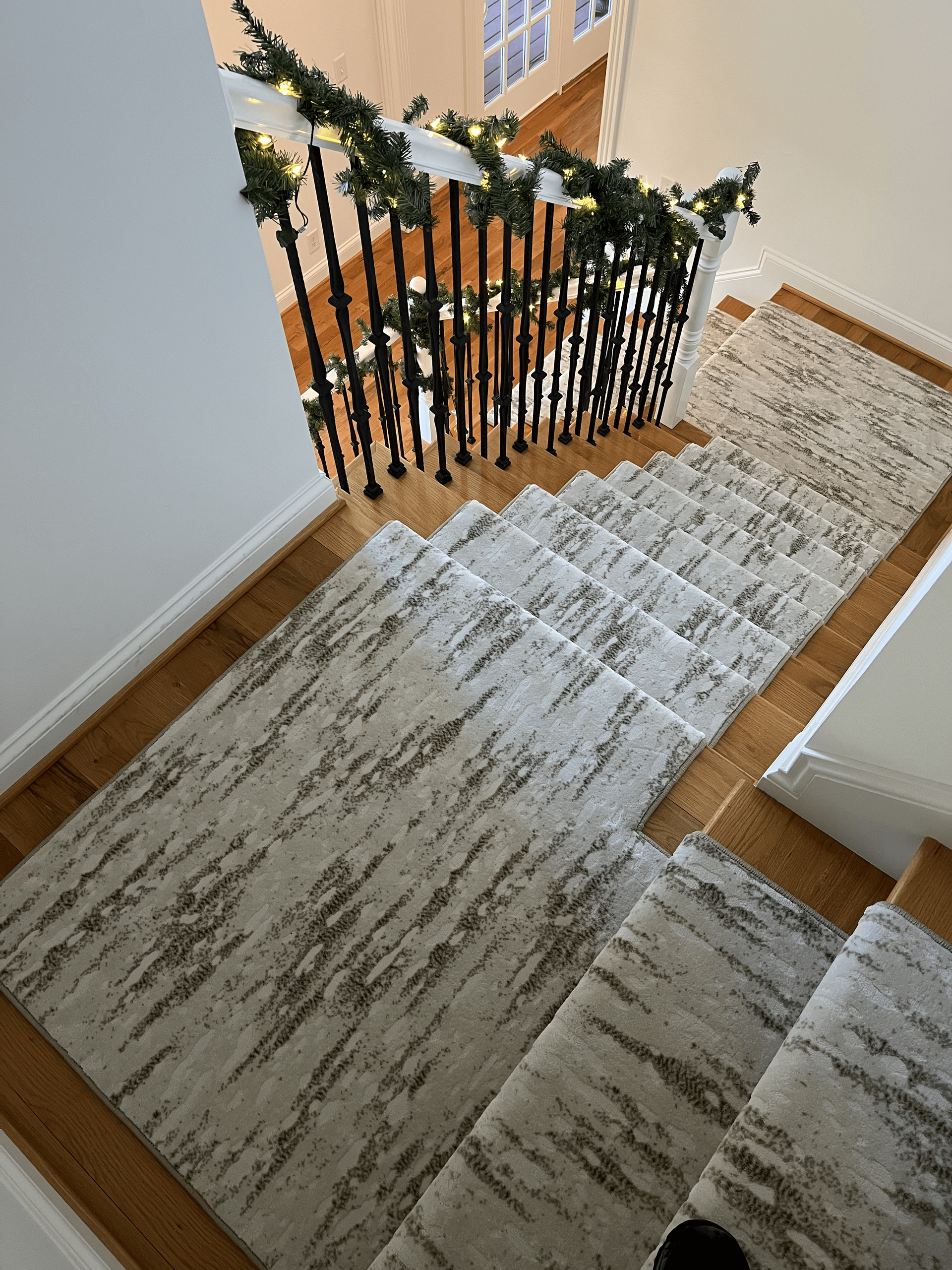 Stair landing with beige runner rug and black banister decorated with white garland and lights