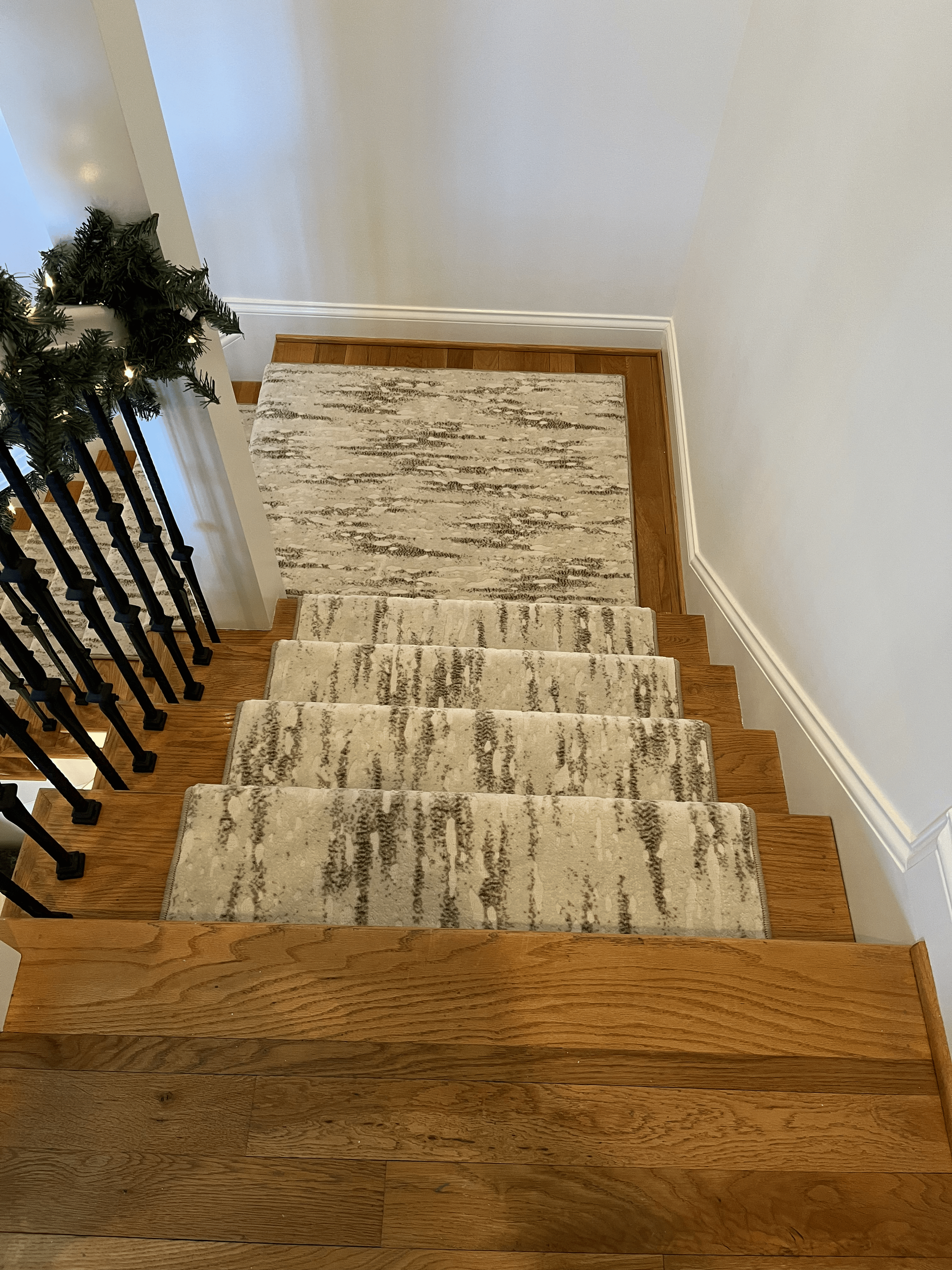 Top of a carpeted staircase with a wooden floor and black railing, viewed looking down.