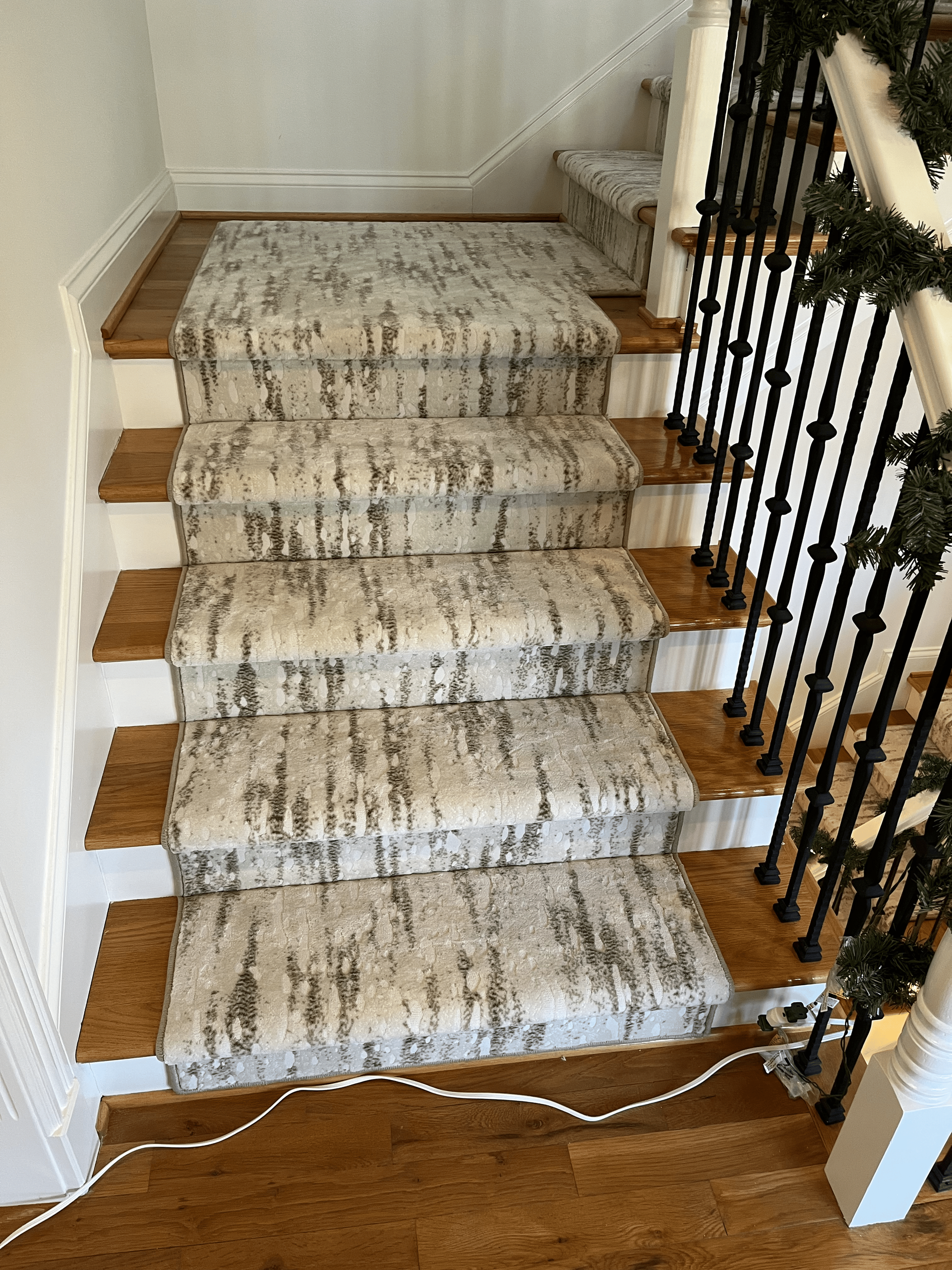 Carpeted staircase with a runner, white walls, and a black railing beside the steps.