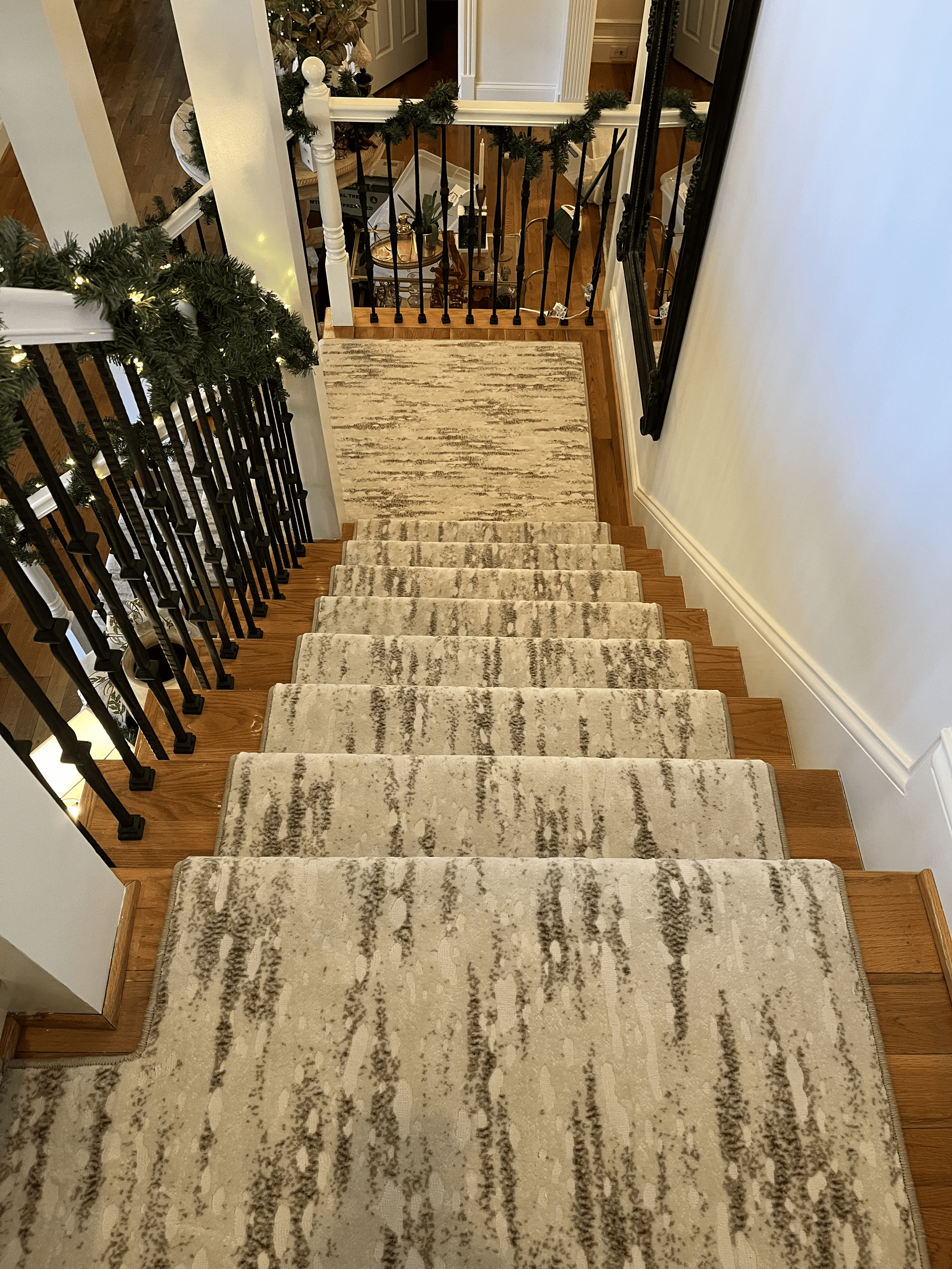 Carpeted staircase with black railings and white walls, decorated with green garland at the landing.