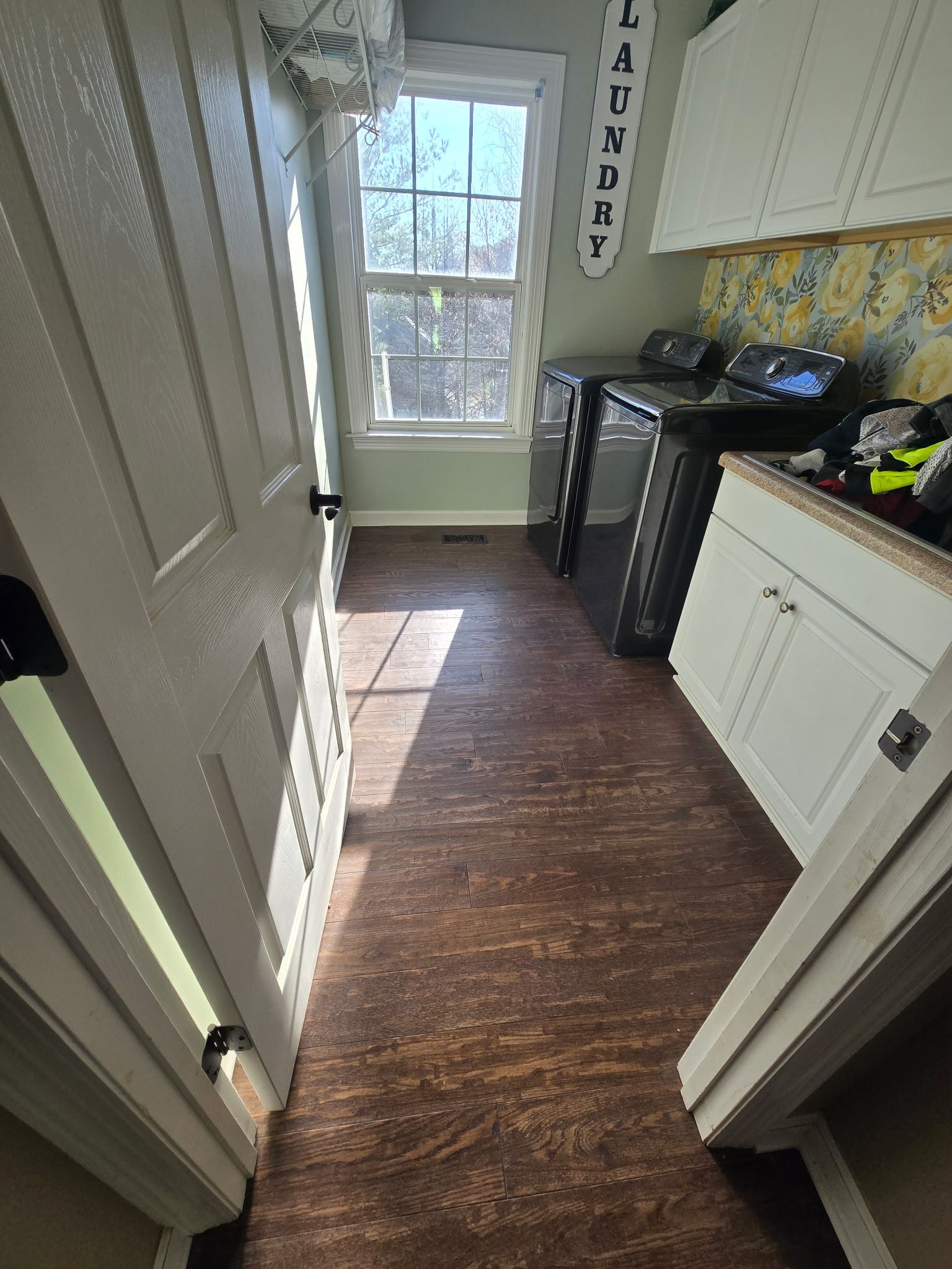 Narrow kitchen hallway with a window, white cabinets, dark wood floor, and a black stove on the right.