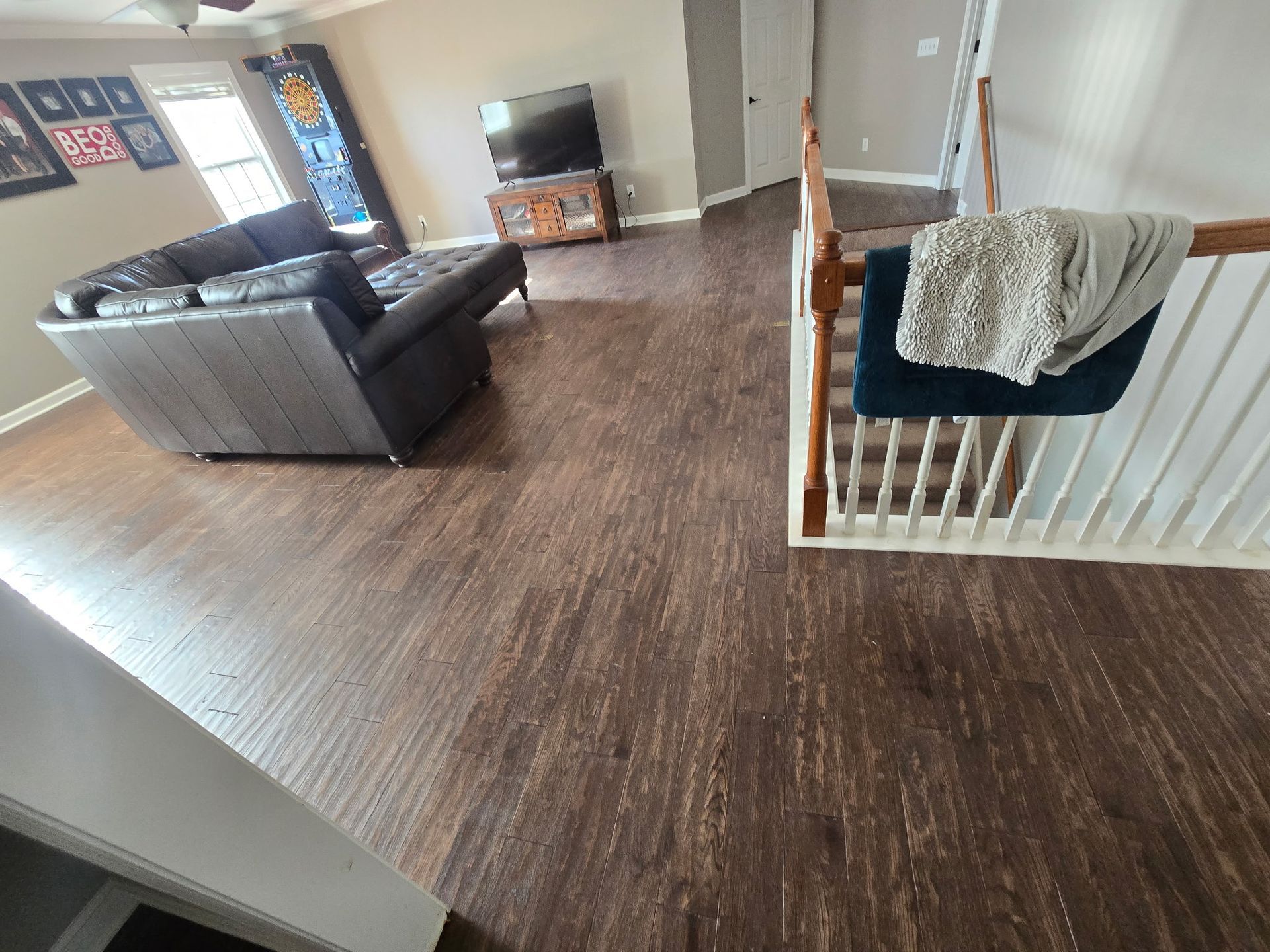 Living room with dark wood floors, gray sofa, TV stand, and a stair railing with a blanket draped over it