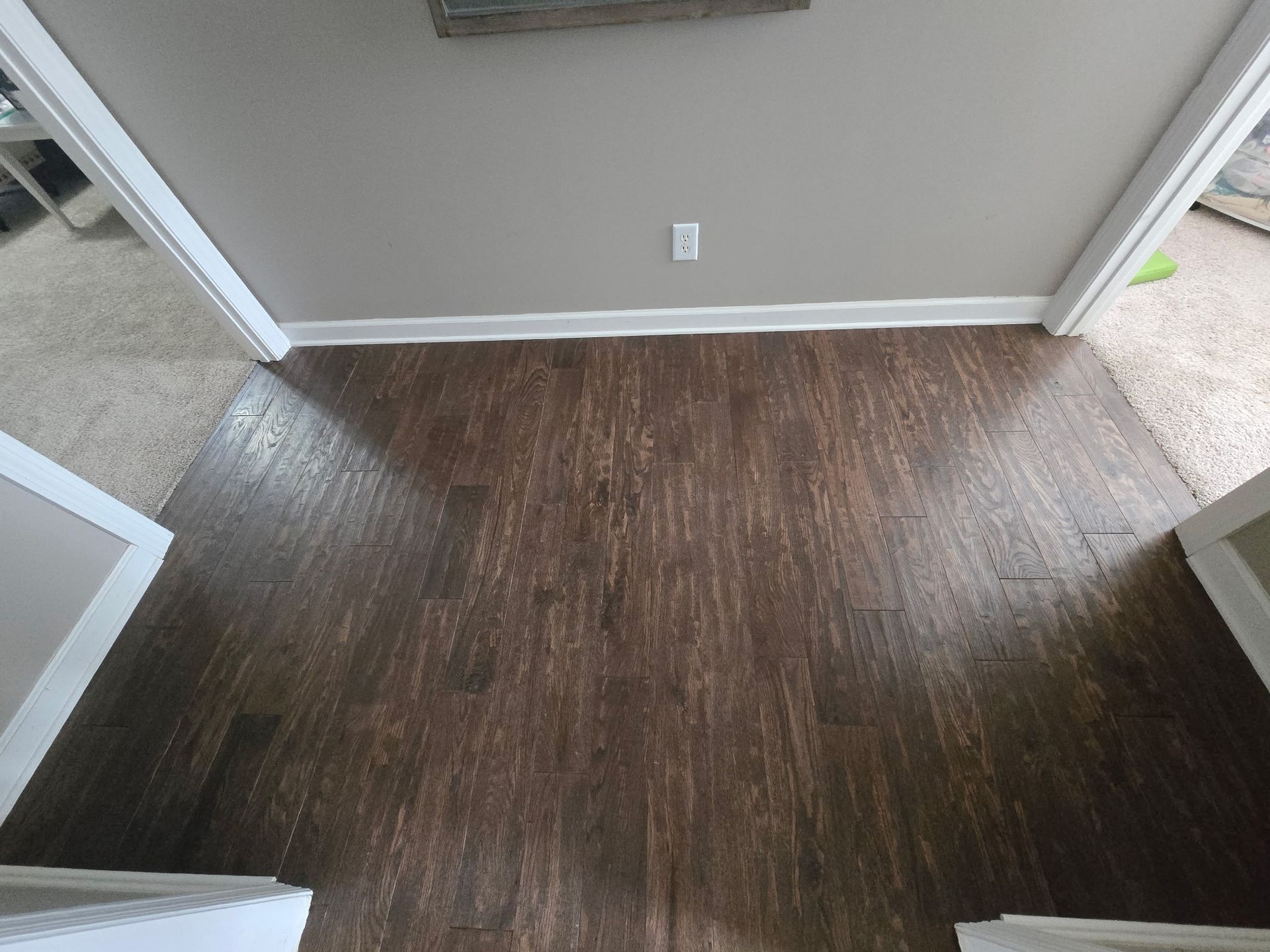 Empty room with dark wood flooring, beige walls, and white trim seen from a doorway.
