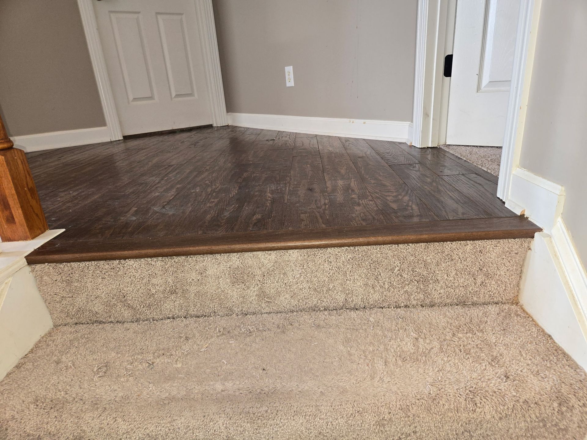 Carpeted step up to a dark hardwood floor in a hallway with white trim and beige walls
