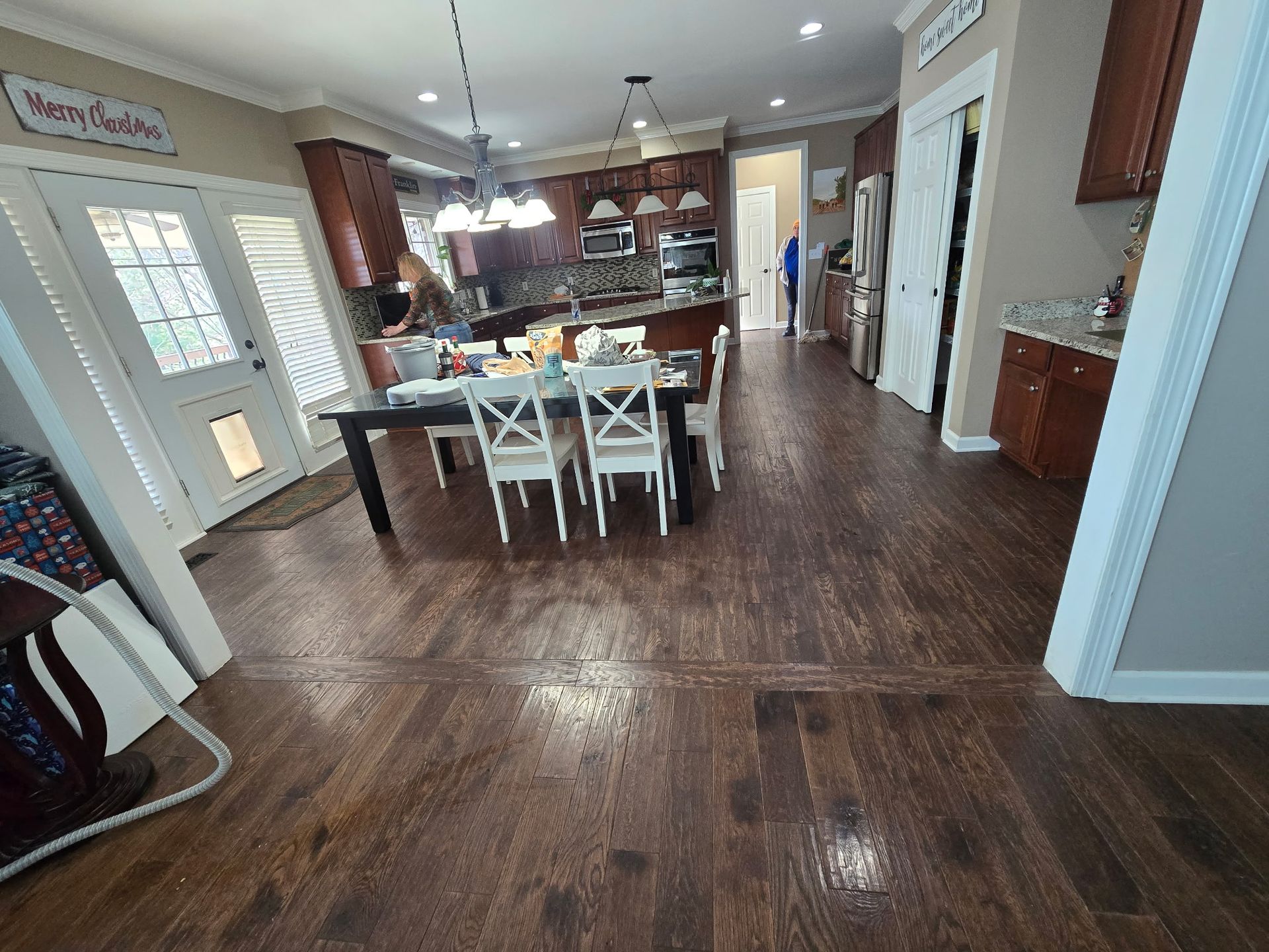 Open kitchen and dining area with dark wood floors, white chairs, island, and hanging lights