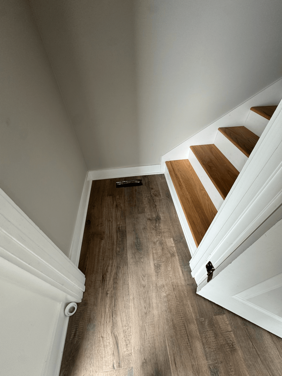 Narrow hallway with wood flooring and a white staircase with wooden steps on the right.