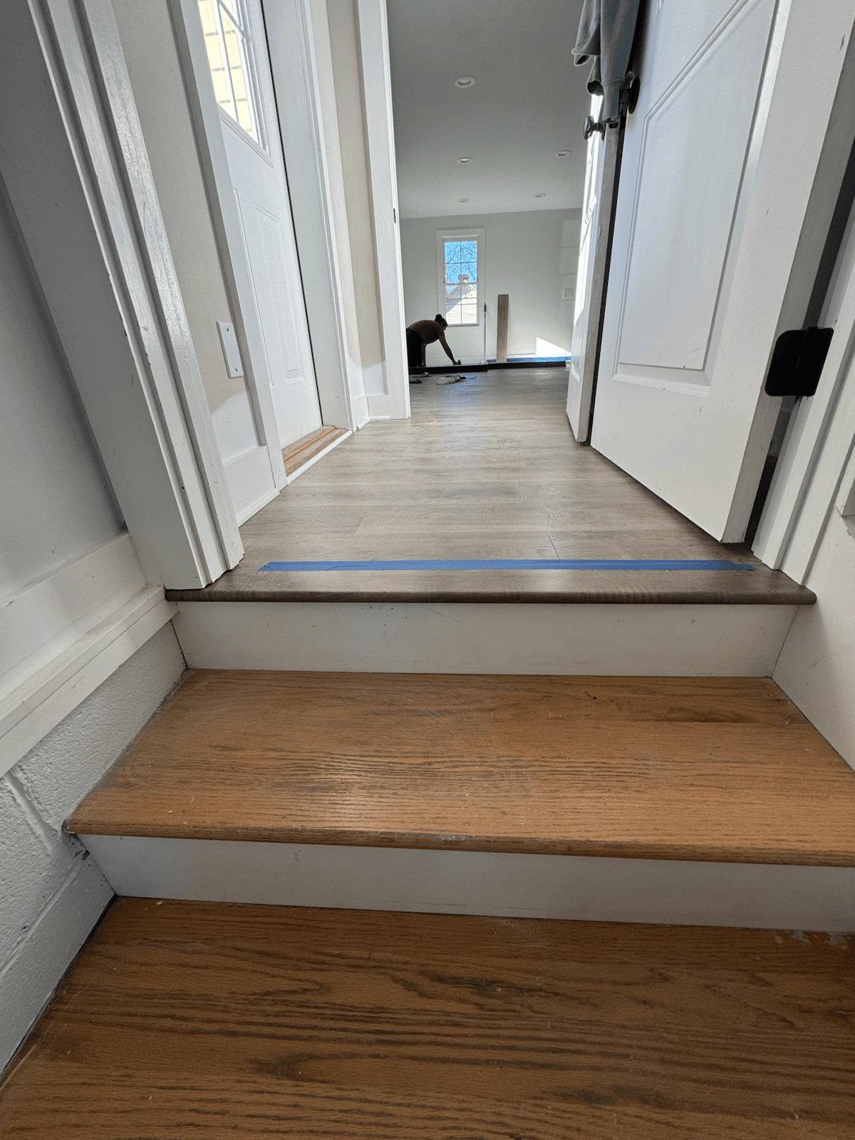 Hallway with two interior steps, white walls, wood floors, and a chair in the distance