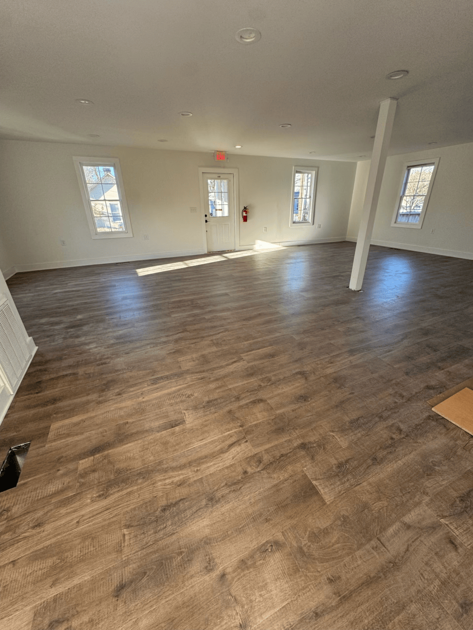 Empty room with wood-look flooring, white walls, windows, and a central support column