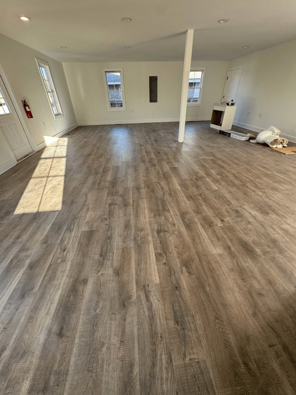 Empty room with wood-look flooring, white walls, windows, and a central support column.